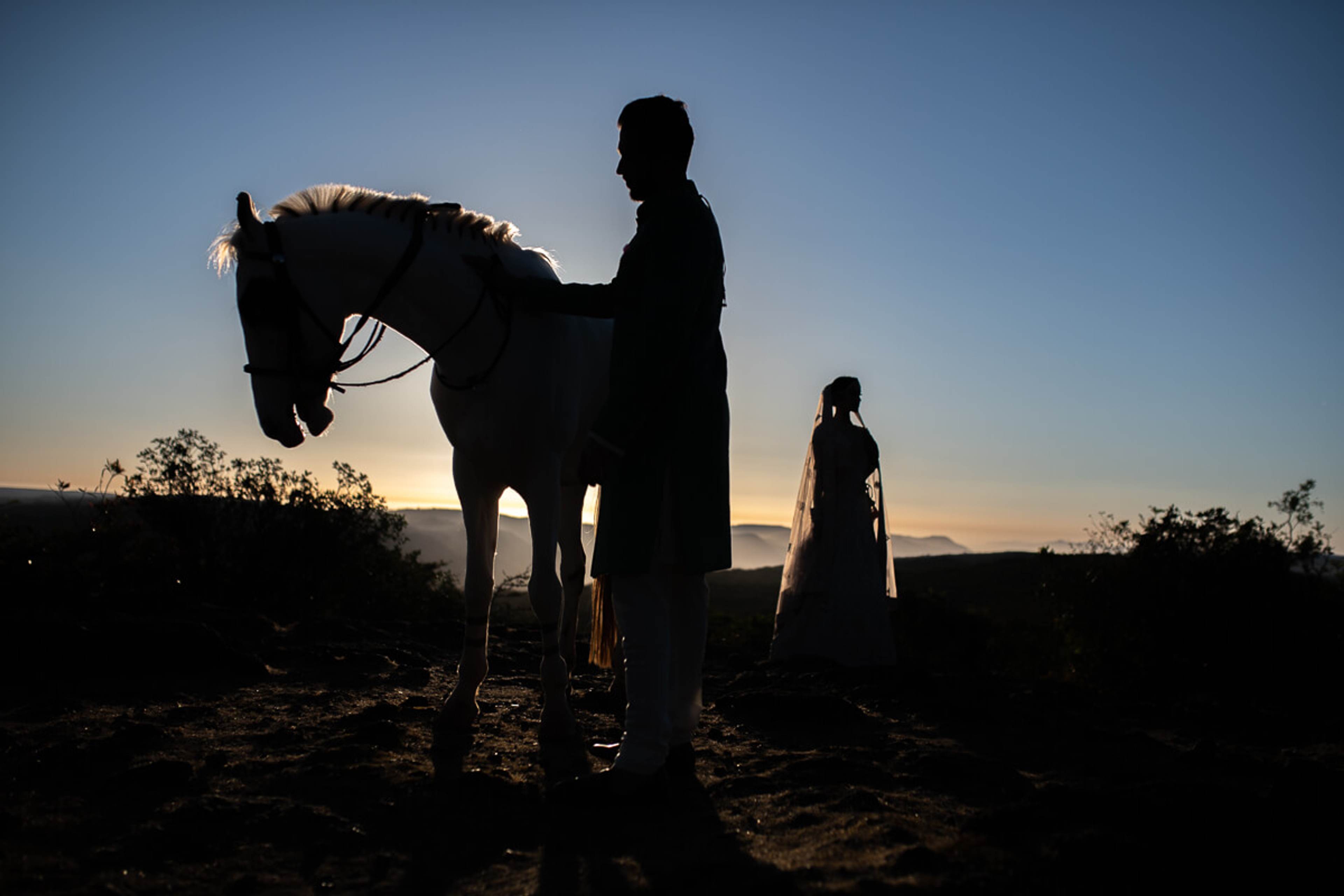 Shreya and Yash silhouetted with horse at sunset in Mahabaleshwar, golden light on horizon