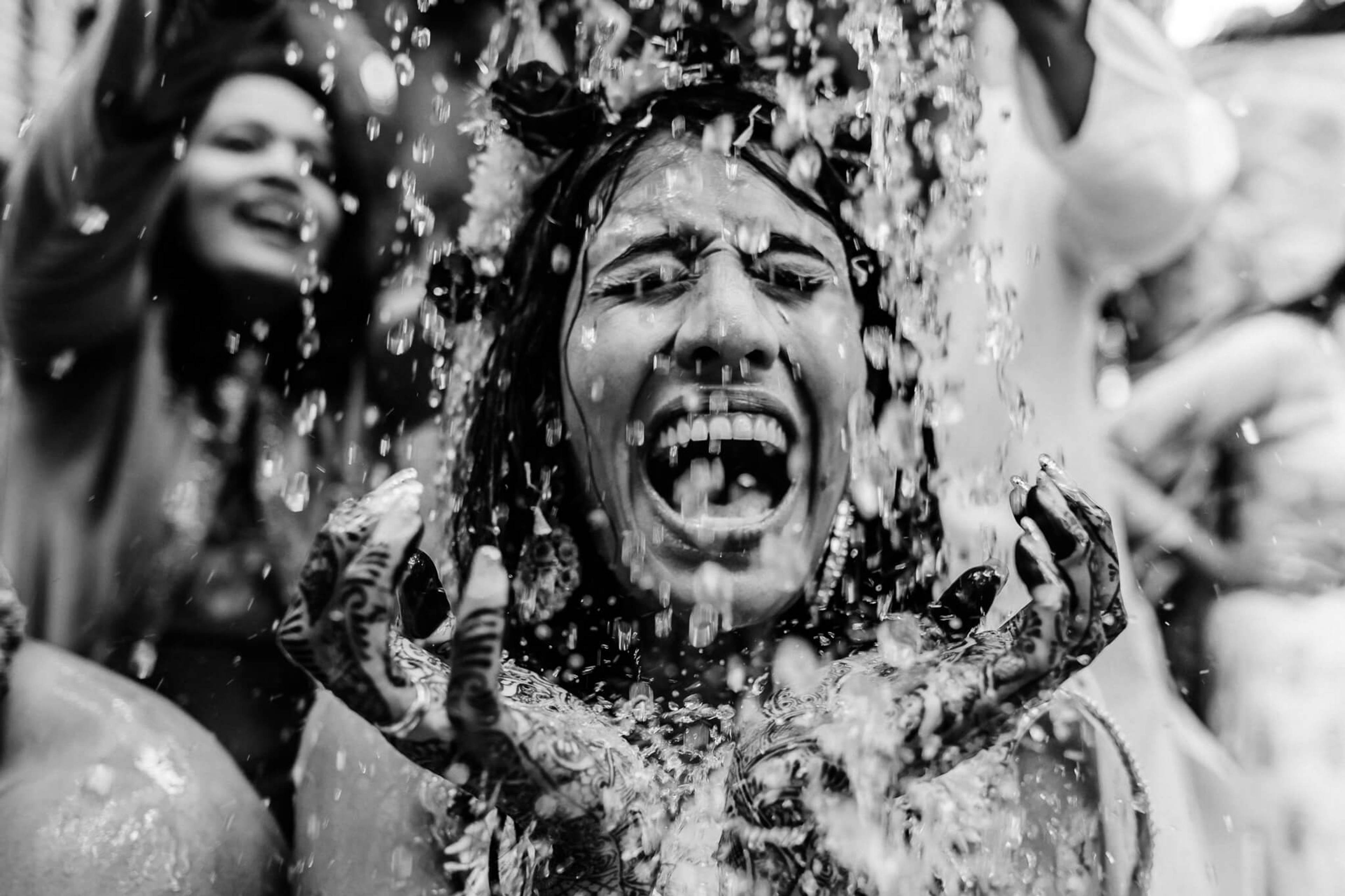 Person laughing with water splashing over their face in black and white candid moment