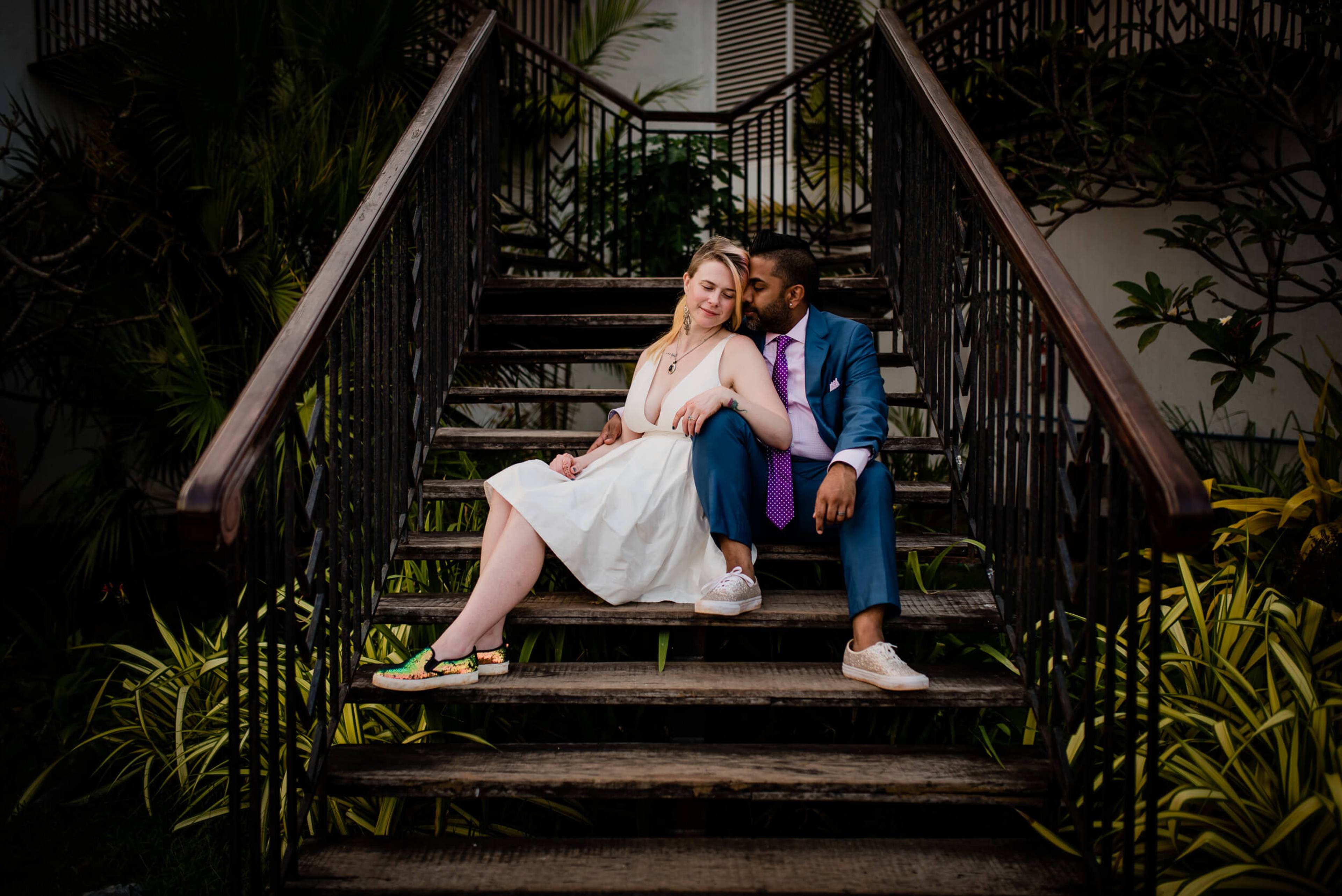 Sarah and Ravin sit together on lush tropical stairs, surrounded by verdant plants in Goa