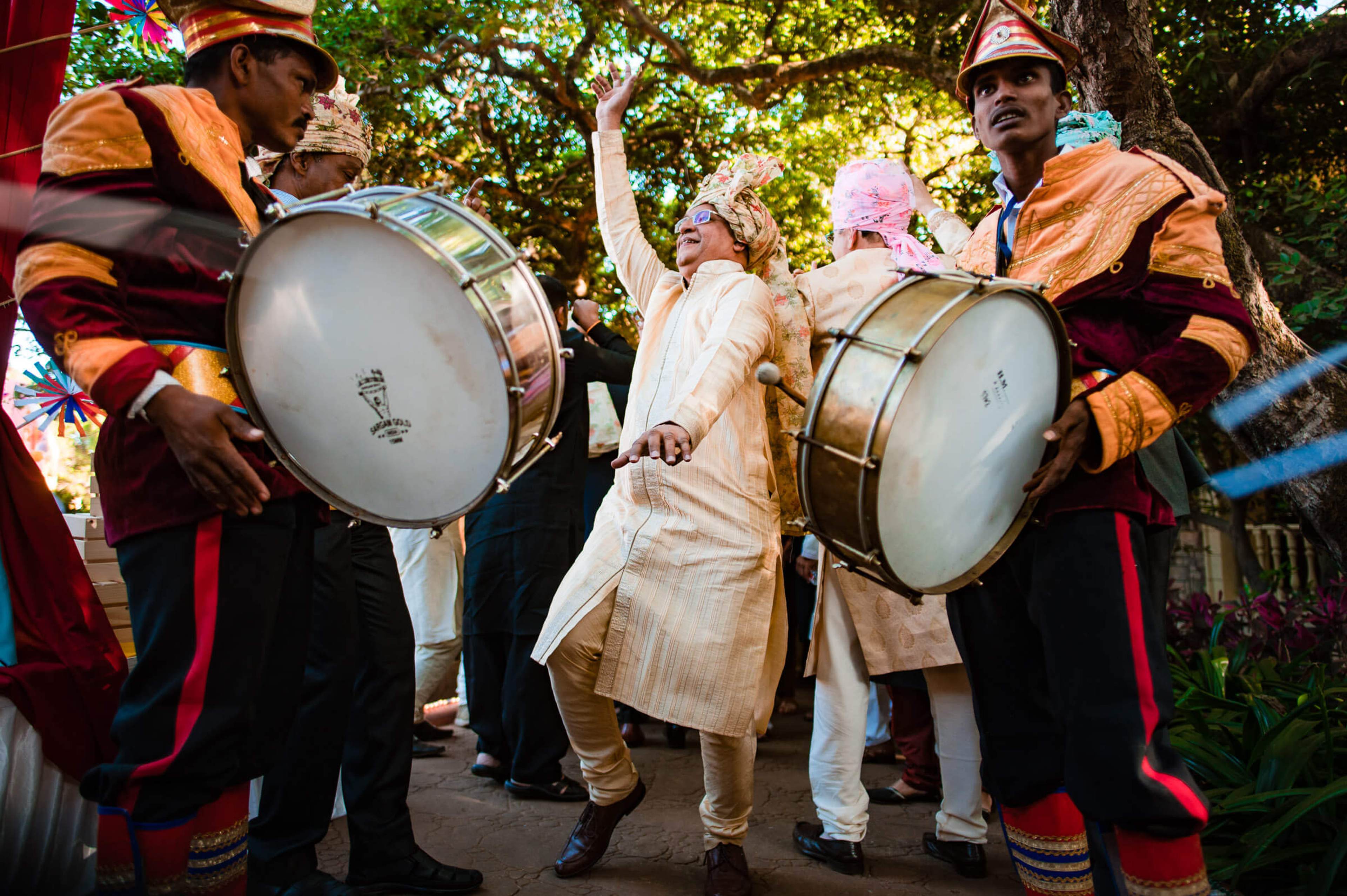 Shreya and Yash celebrate with traditional drummers in colorful attire at Mahabaleshwar, dancing under sunlit trees