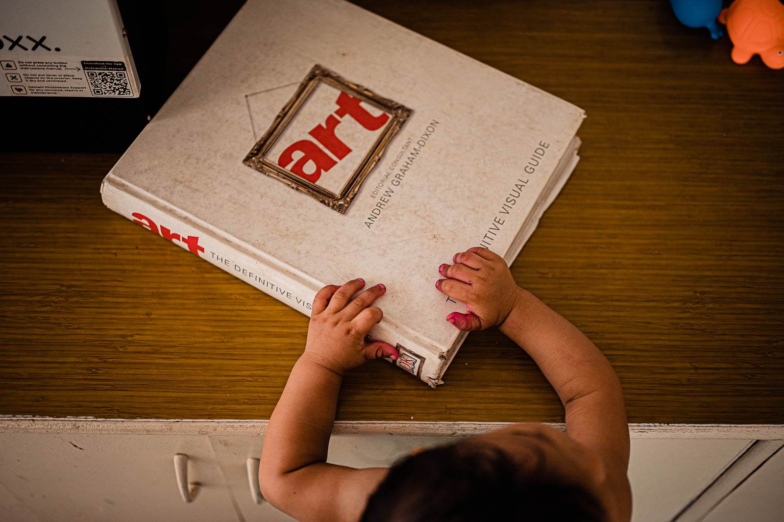 Child's hands reaching for a red-covered book on a wooden table