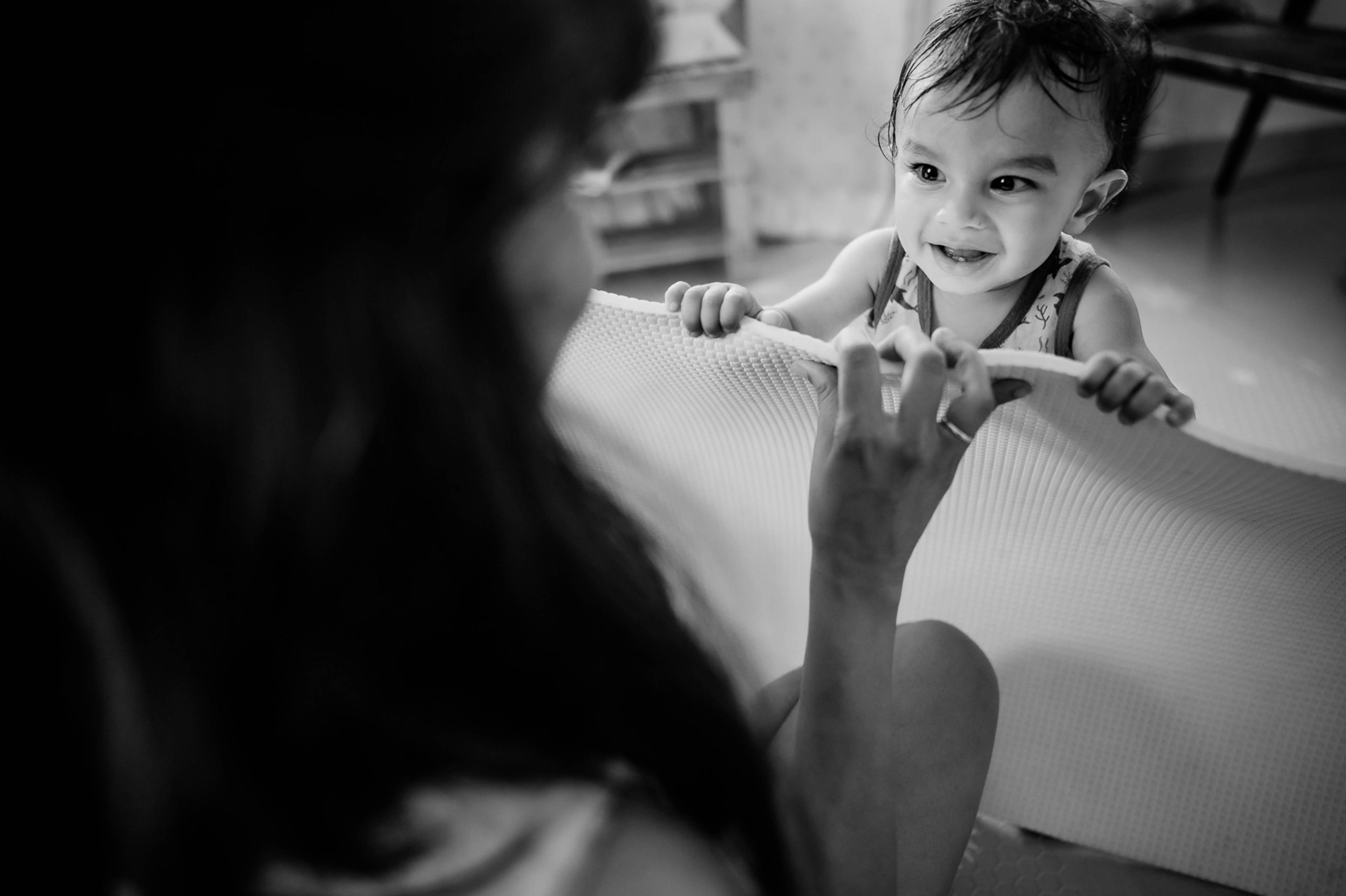 Toddler smiling at camera while playing with adult in black and white interior shot