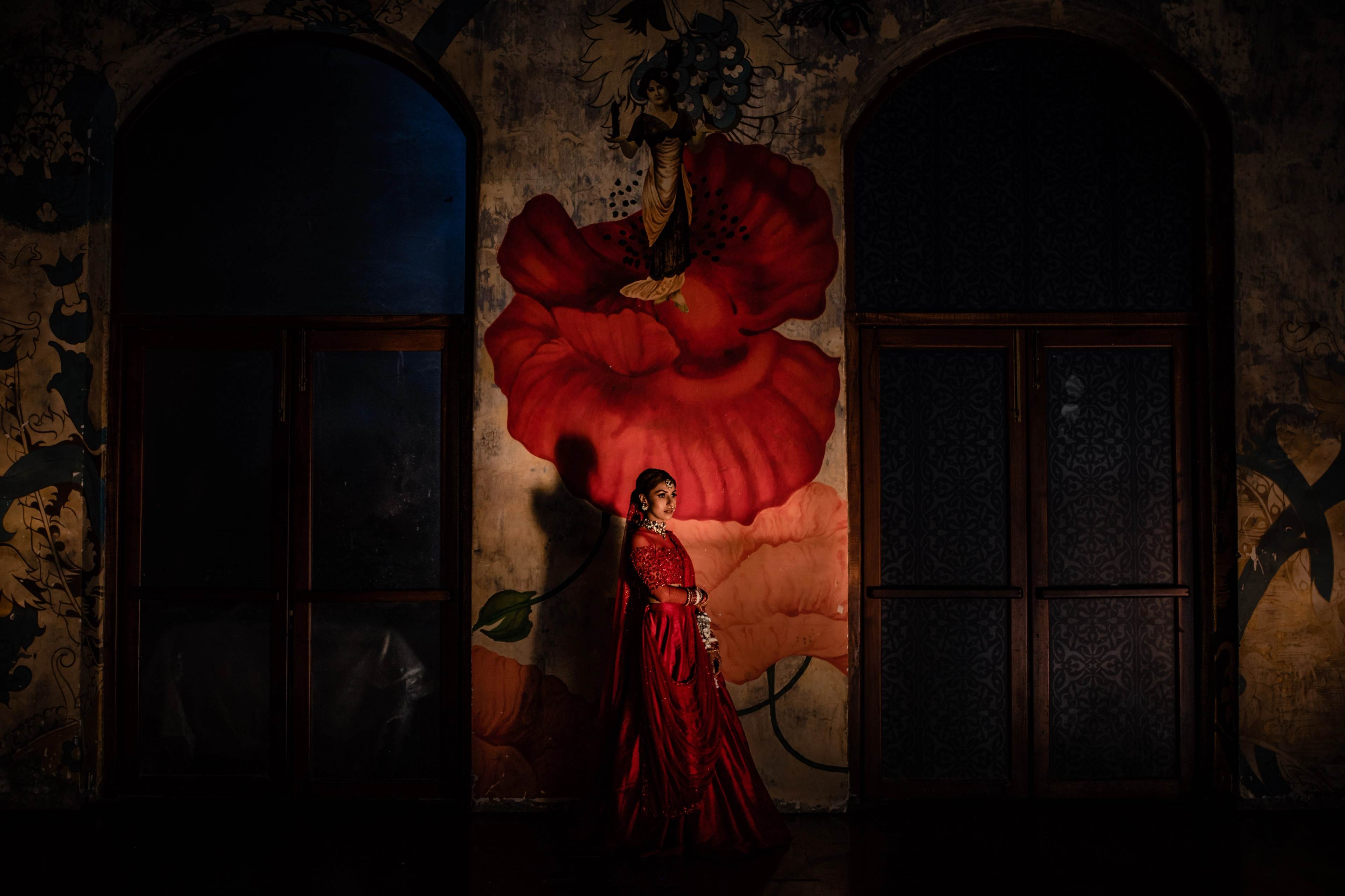 Woman in red flowing gown posed against dramatic poppy mural in vintage archway setting