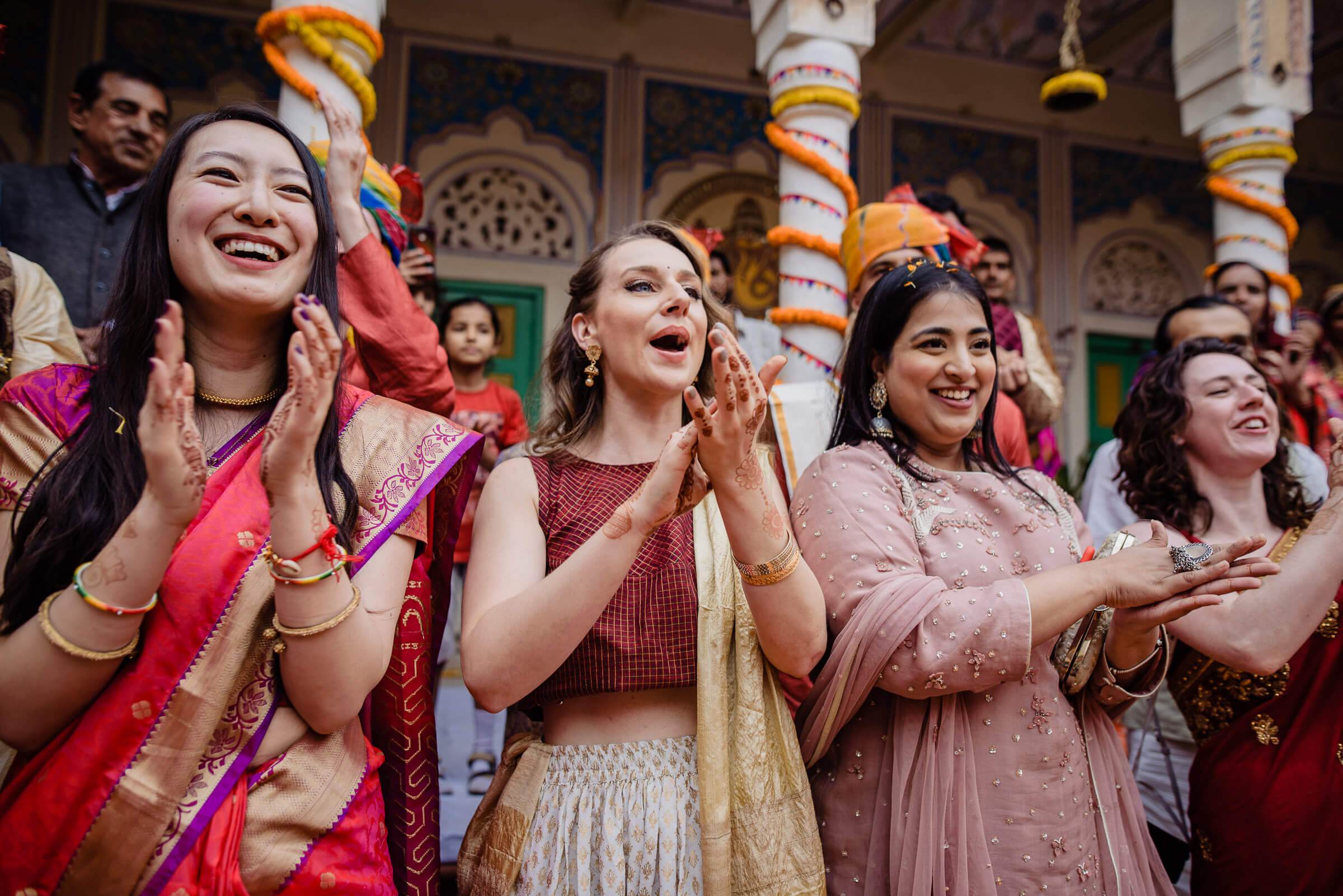 Women in colorful traditional attire celebrating at a decorated temple in Rajasthan, clapping and smiling joyfully