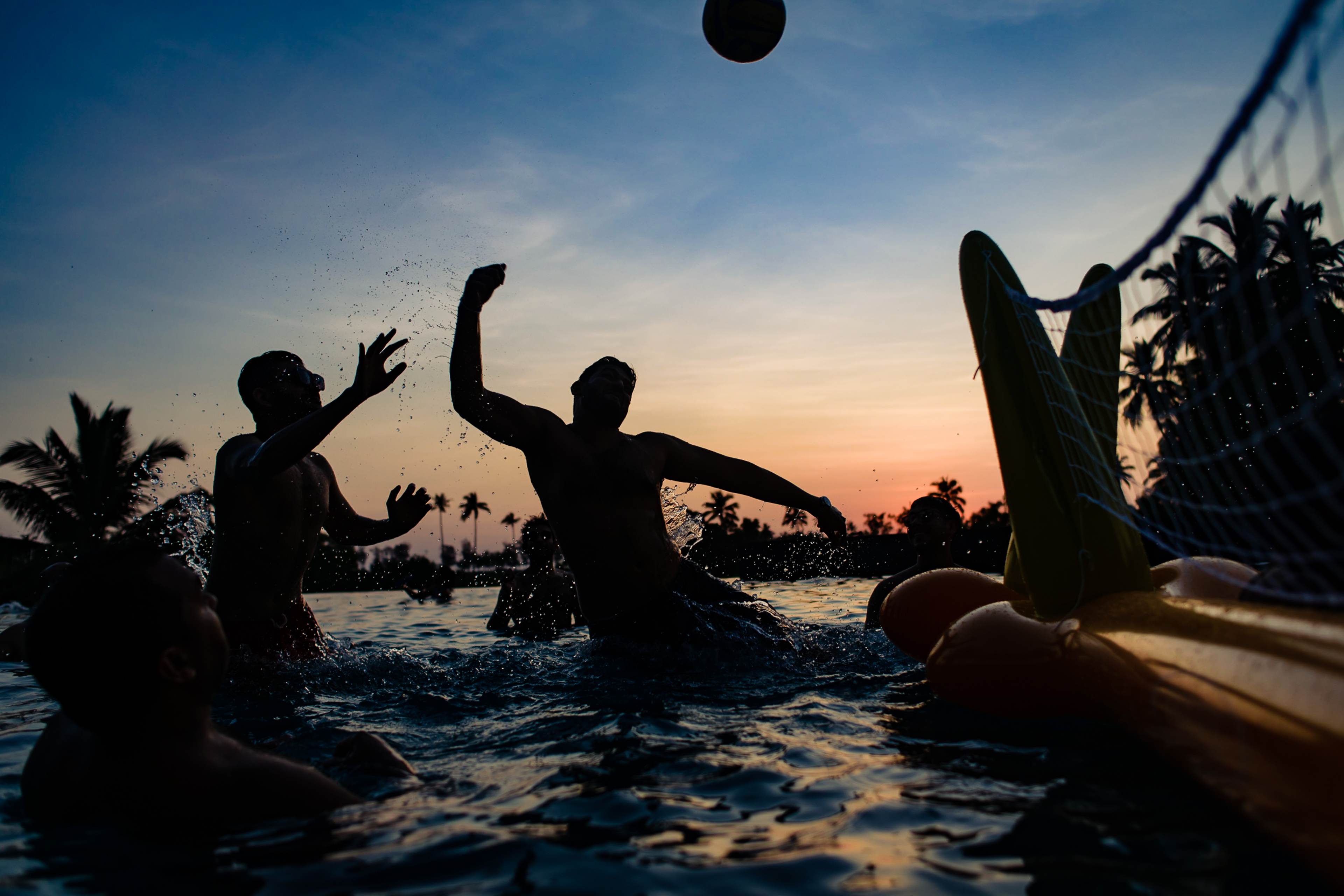 Avani and Srikant play volleyball in the ocean at sunset in Goa, silhouetted against golden light