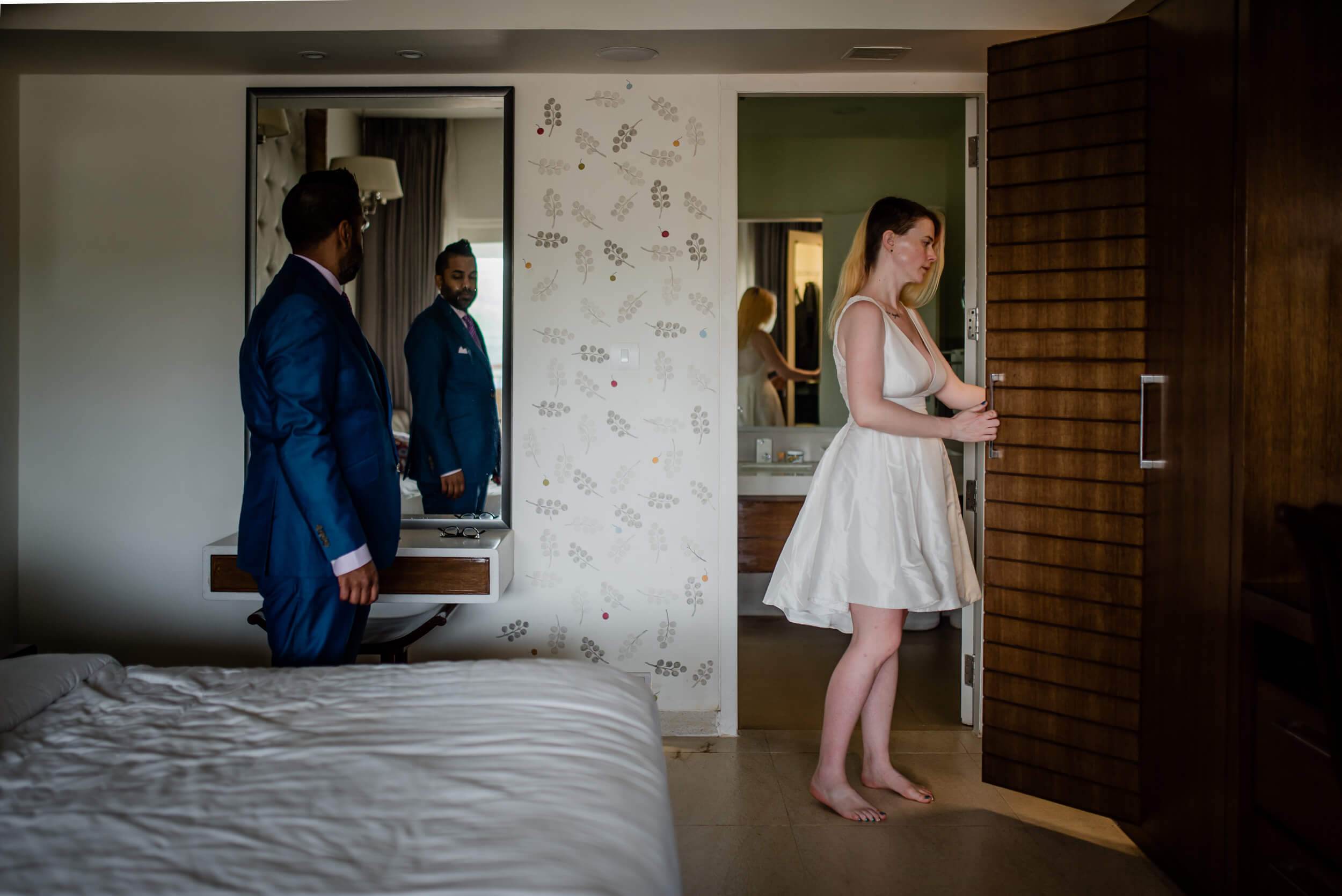 Sarah in white dress and Ravin in blue suit prepare in bedroom during Goa wedding morning