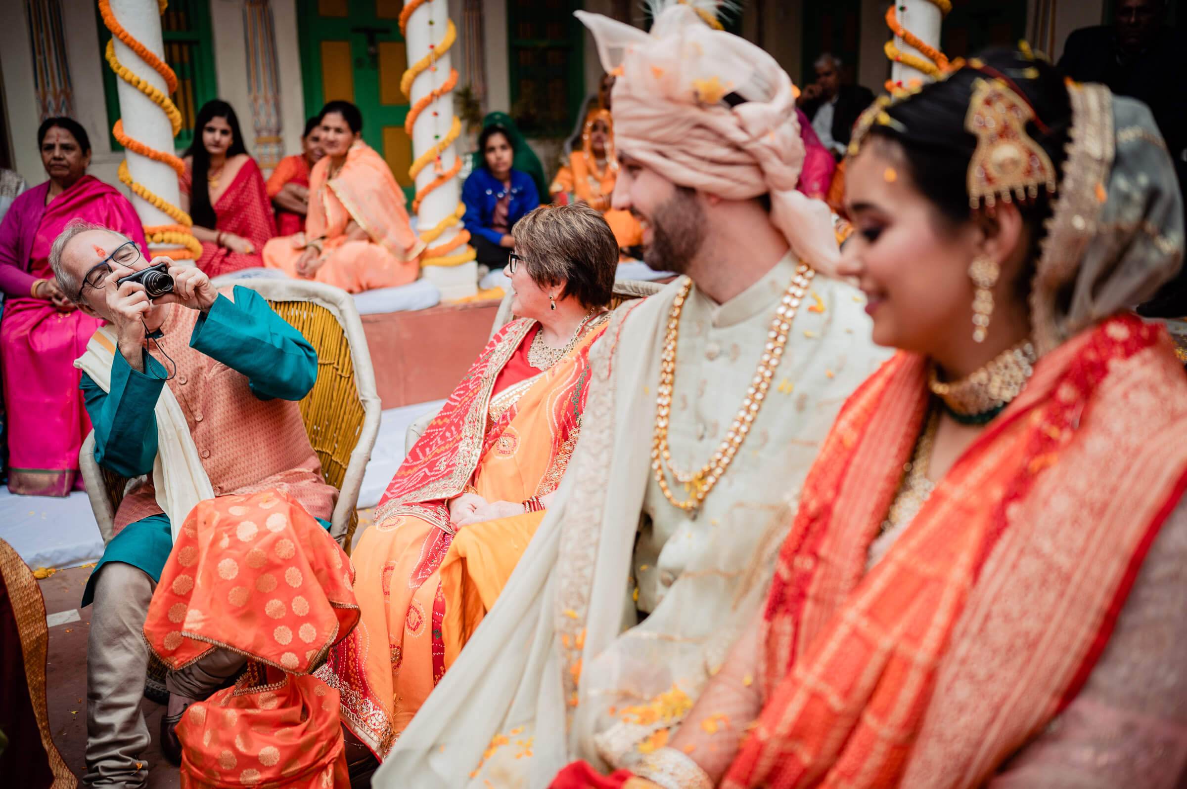 Maitrayee and Eric in traditional Indian wedding attire at a Rajasthan ceremony, surrounded by family and guests
