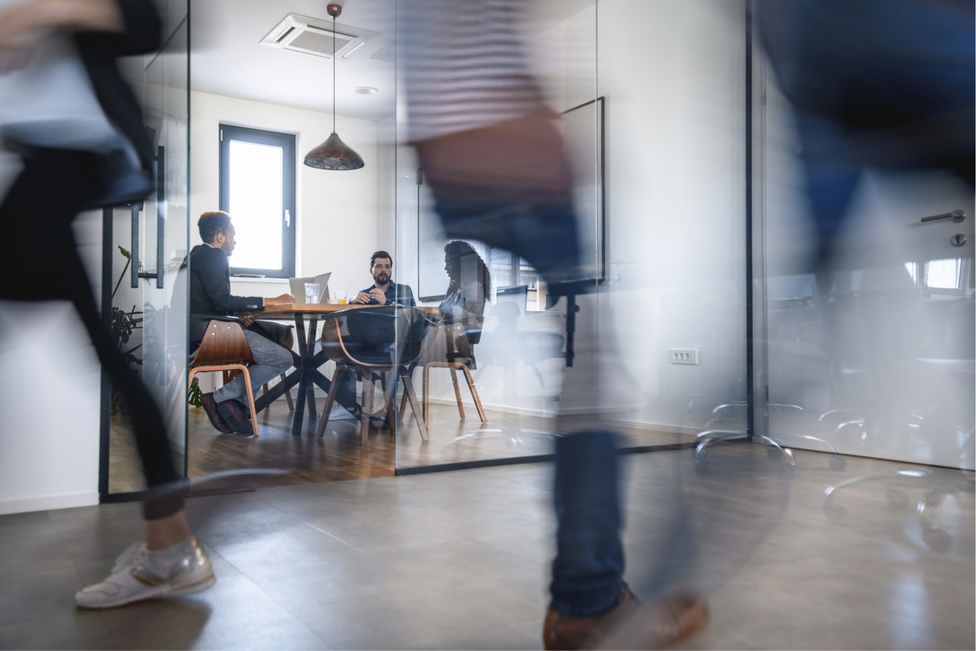 Office with a glass conference room. Three people deep in conversation, blurred figures in the foreground.