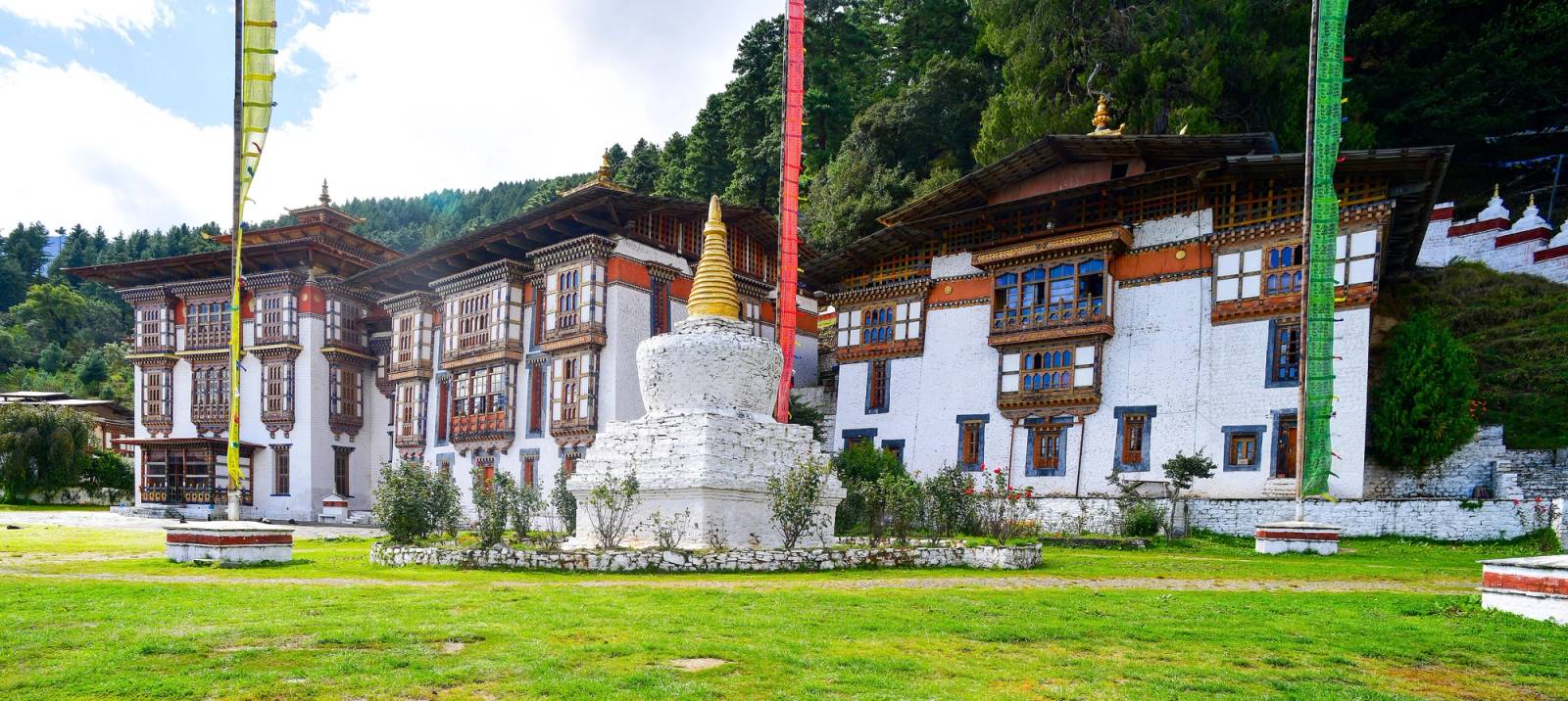 Kurjey Lhakhang's temples and a white chorten with a gold spire, prayer flags on the lawn