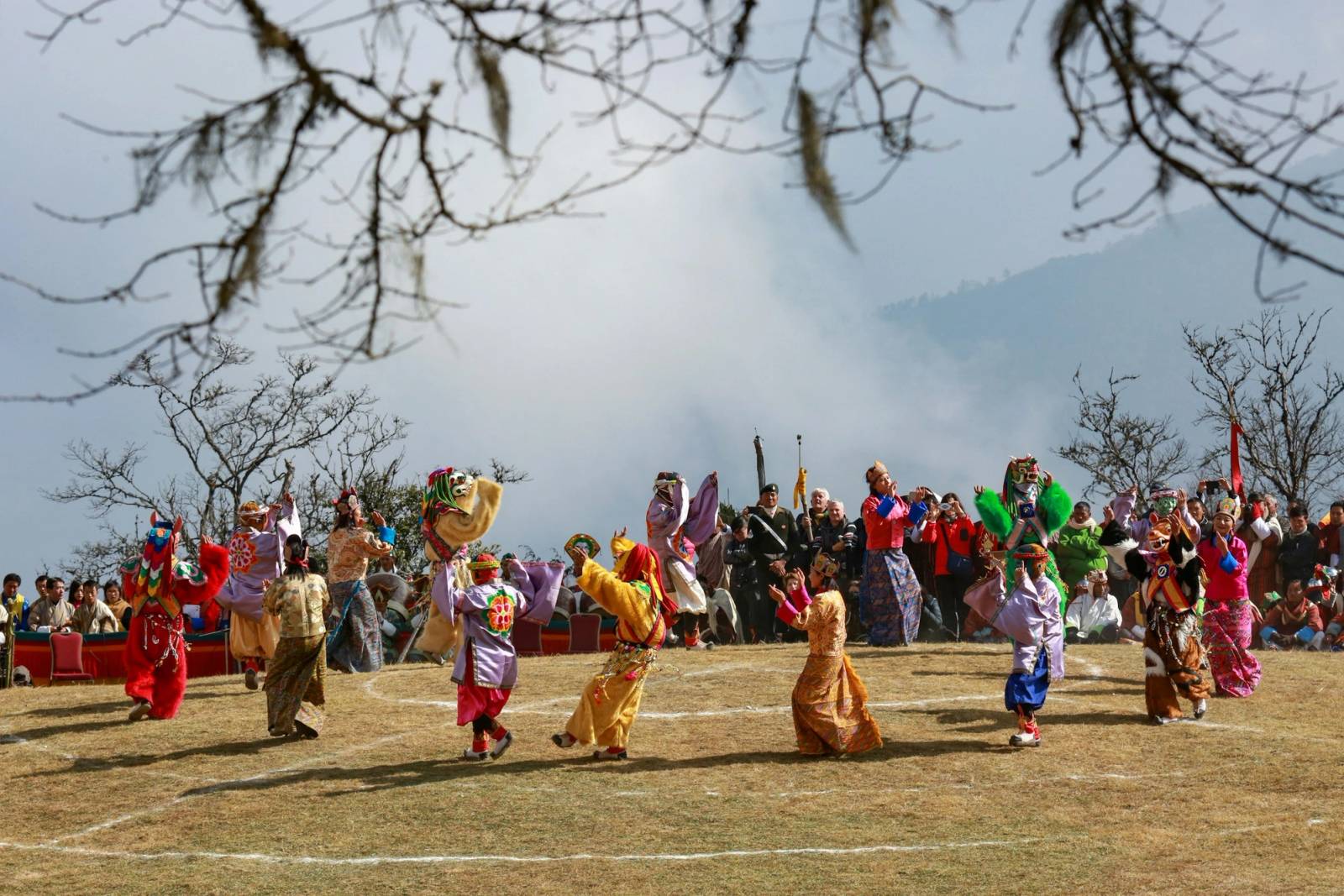 Masked dancers in bright costumes circle an open festival ground as a crowd looks on