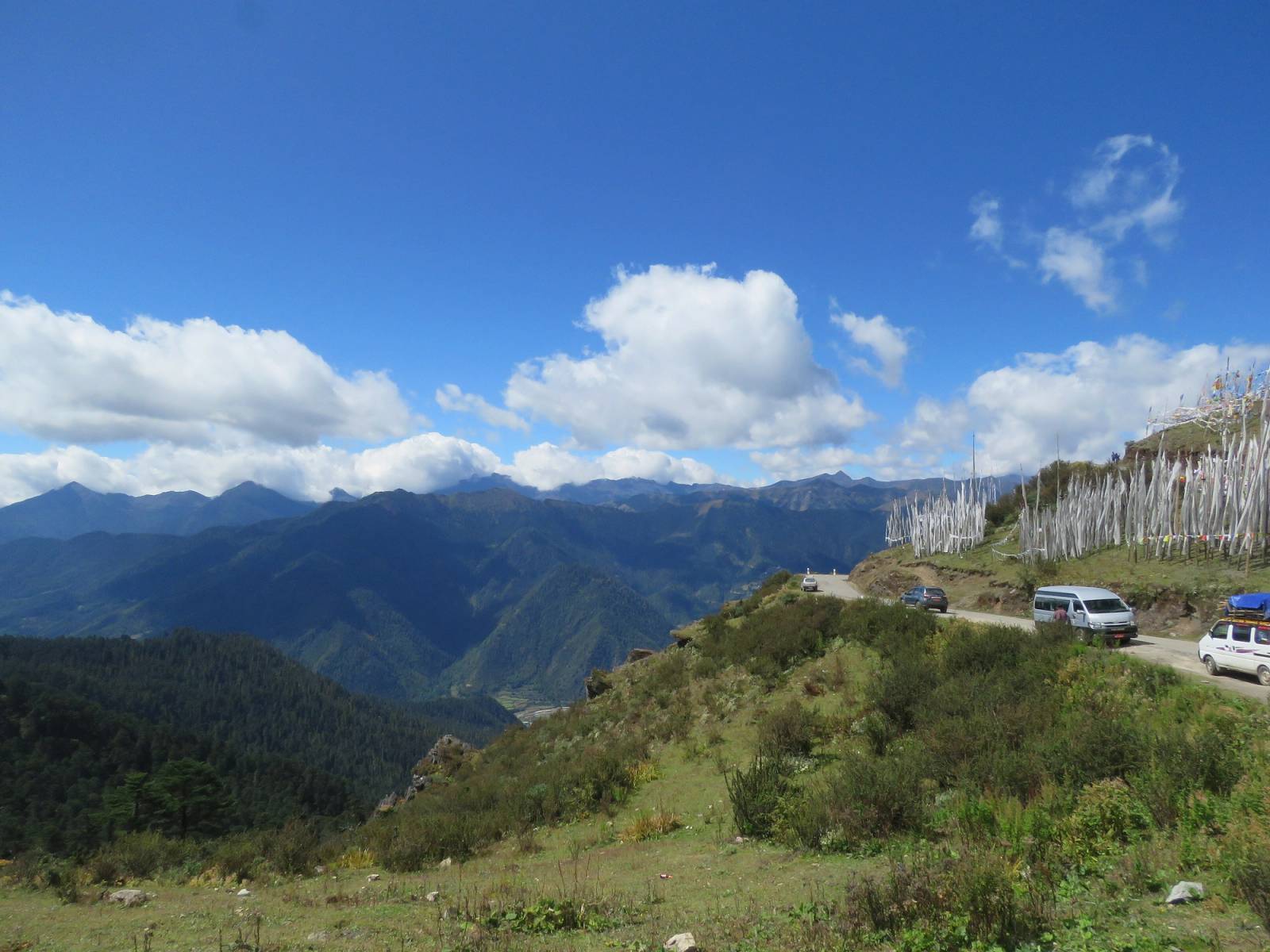 Cars on the road over Chele La, with white prayer flags and blue mountain ridges beyond