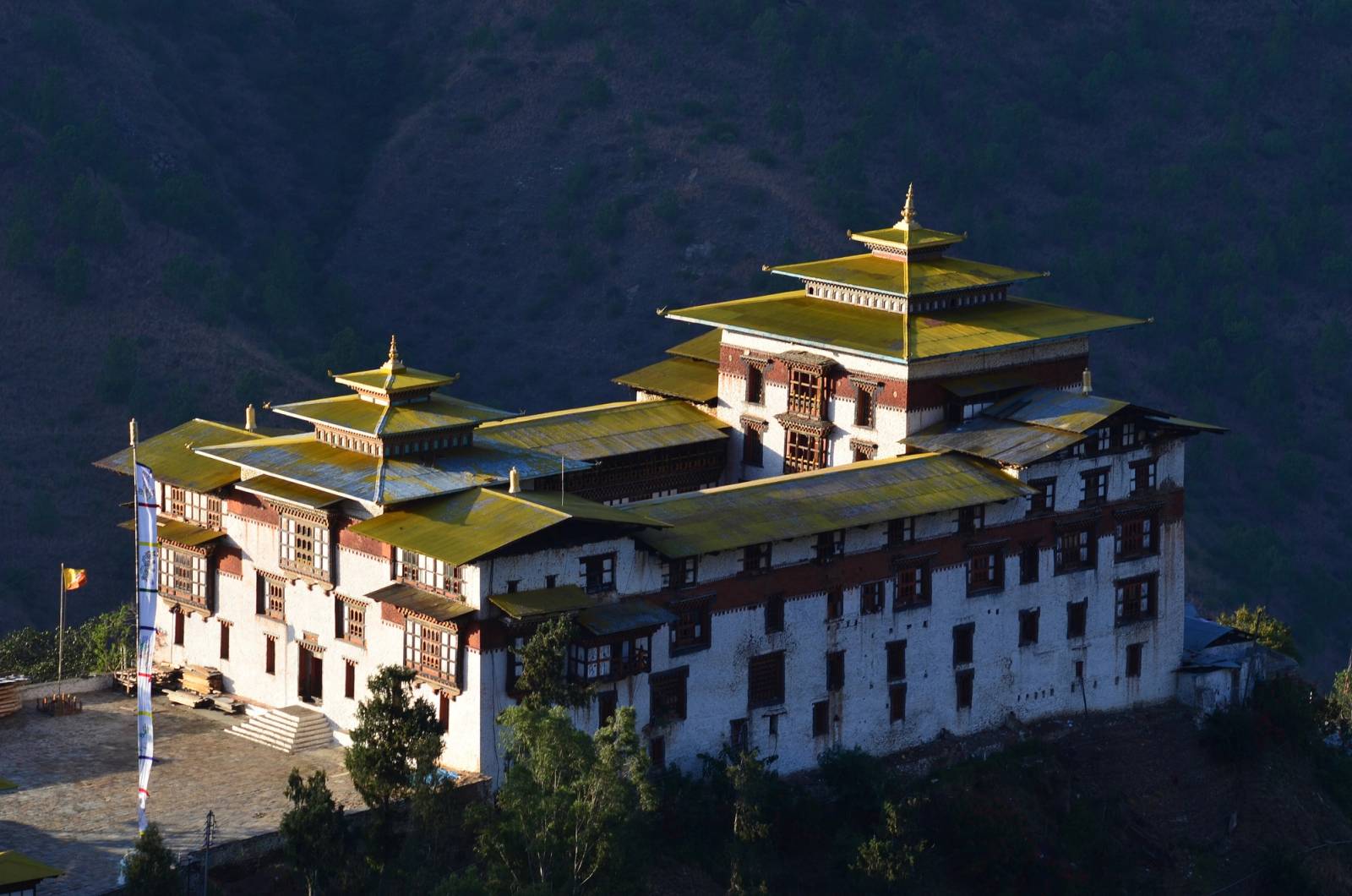Trashigang Dzong's white walls and yellow roofs lit by low sun against a dark hillside