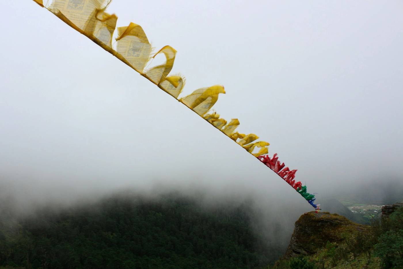 A string of prayer flags stretched over a misty cliff edge above forest