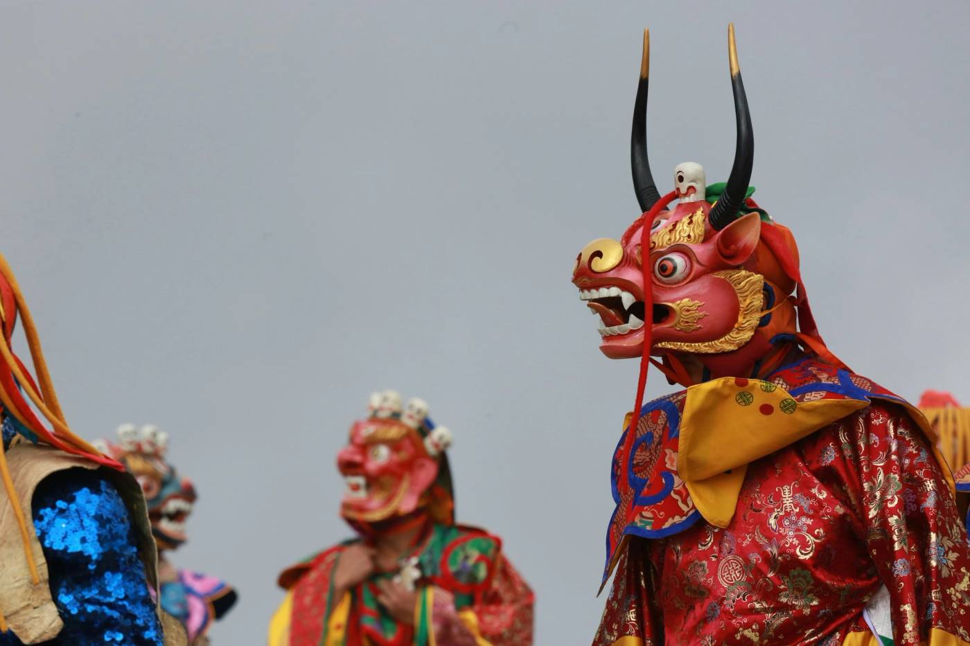 Masked tshechu dancers in red silk, one mask with horns and bared fangs