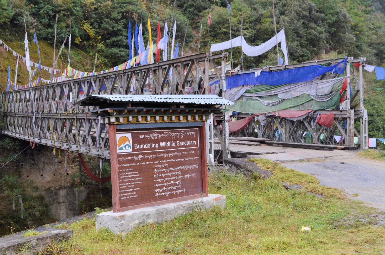 The Bumdeling Wildlife Sanctuary signboard beside the prayer-flag-hung bridge into the sanctuary