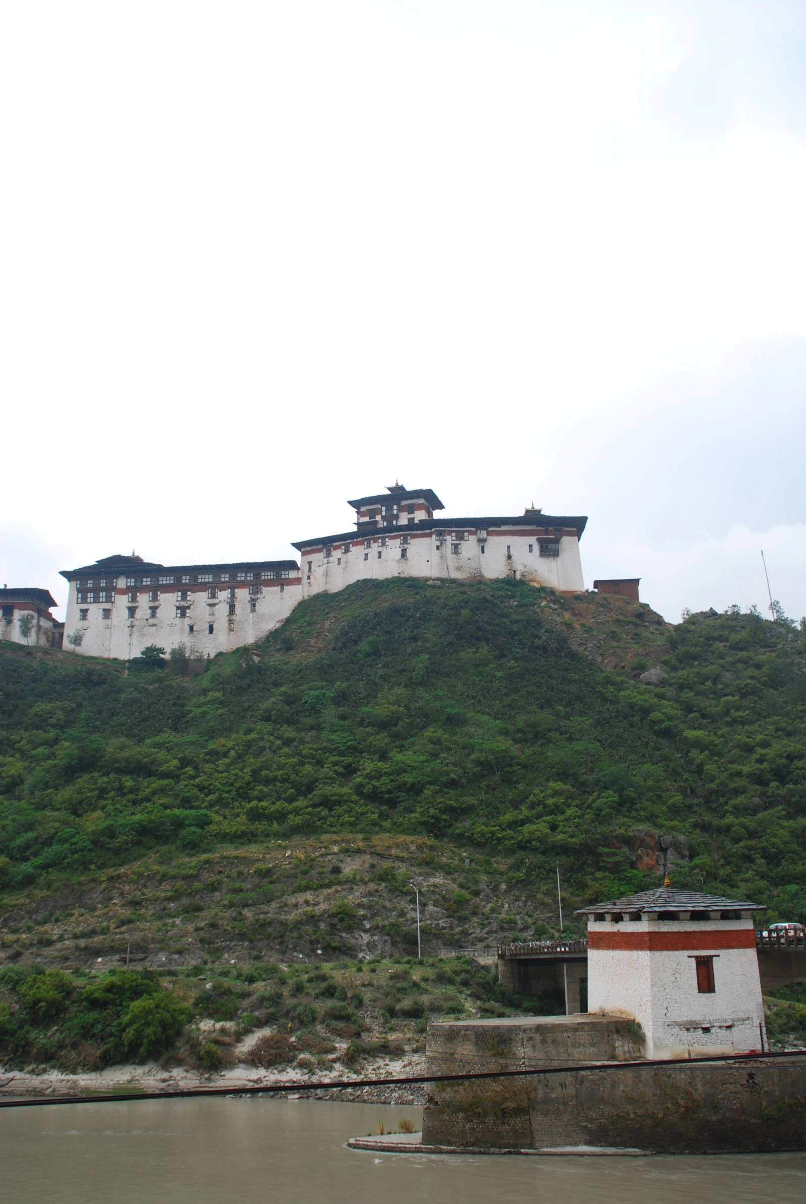 The small white chorten with a red band on its stone base beside the Wangdue road bridge, the dzong on the ridge above
