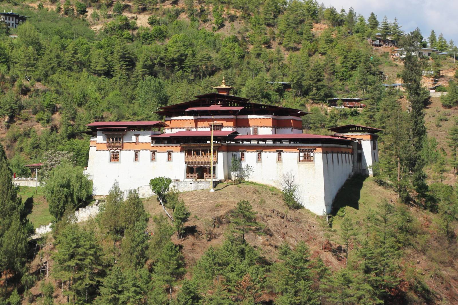 Simtokha Dzong, white walls under red roofs, on its pine-covered ridge above the Thimphu valley