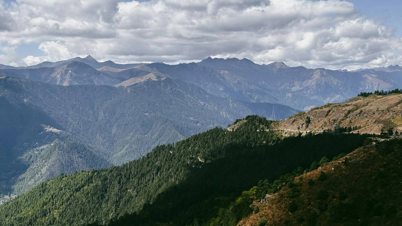 Layered mountain ridges and pine forest under a cloudy sky