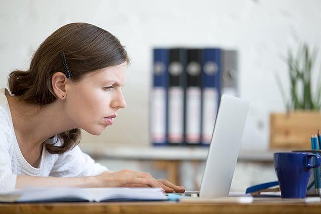 En kvinne lener seg tett inntil skjermen på en laptop mens hun myser