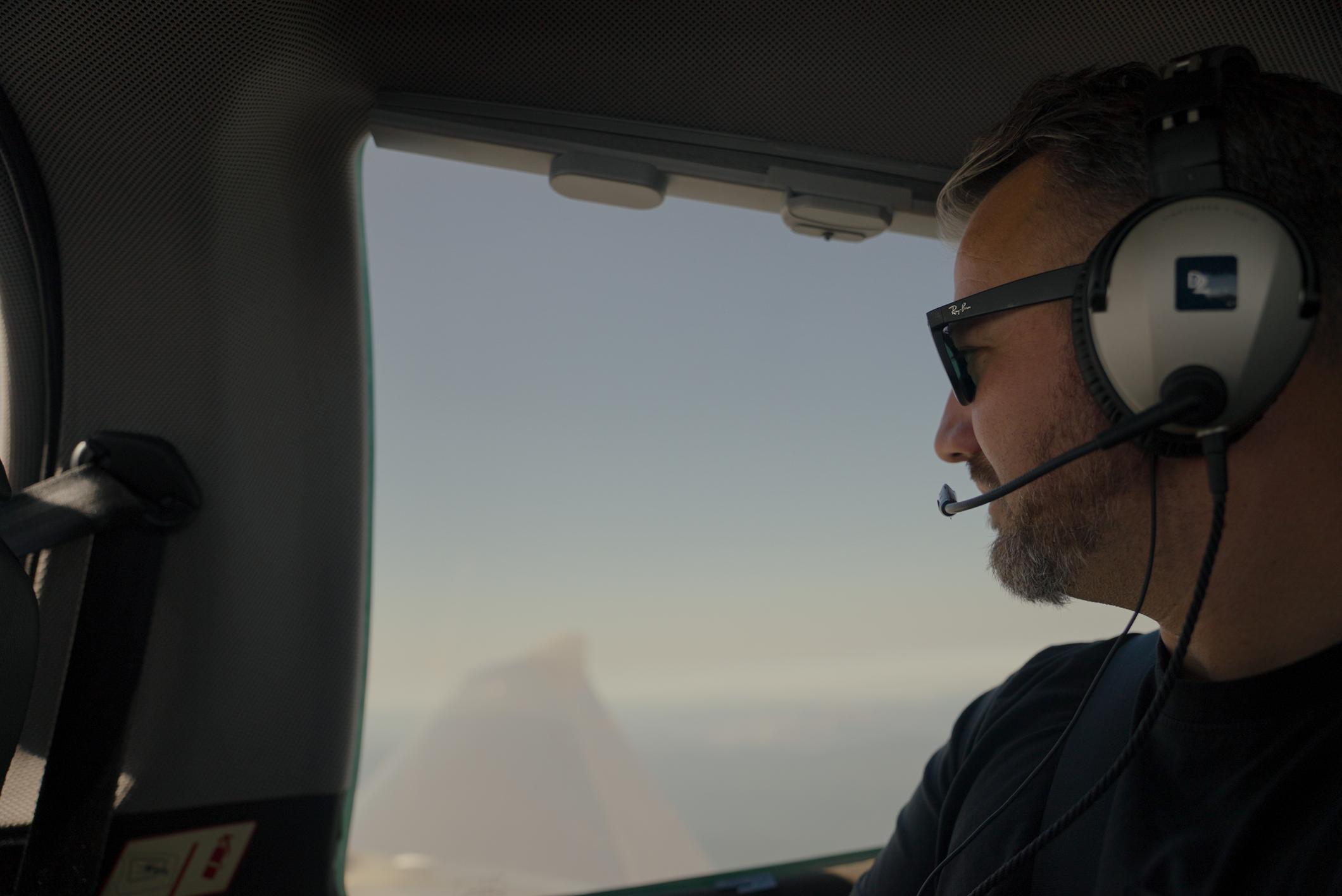 Man in an aircraft looking out of a window over the wing of a plane