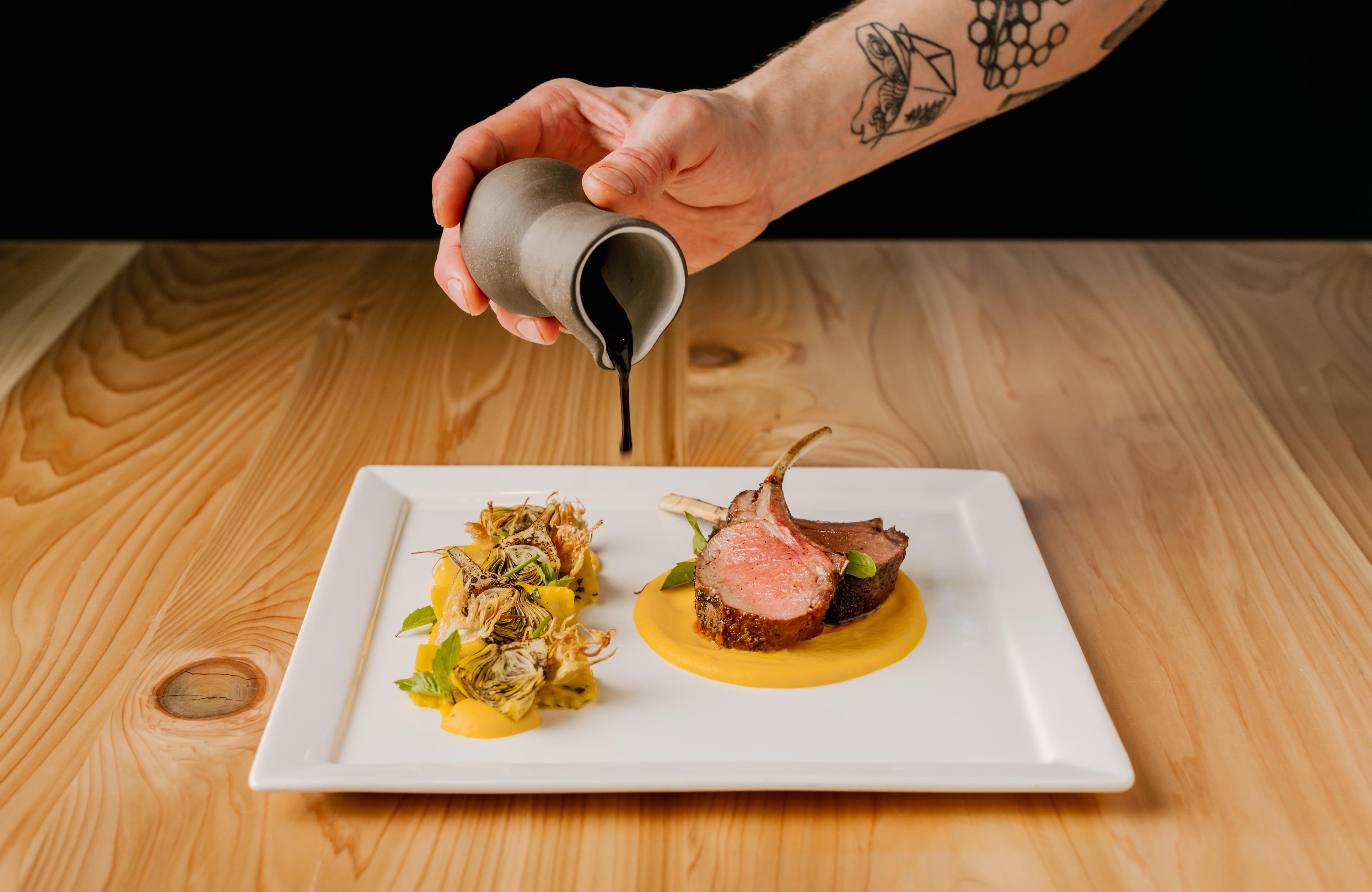 Plate of food with hand pouring a sauce over the top