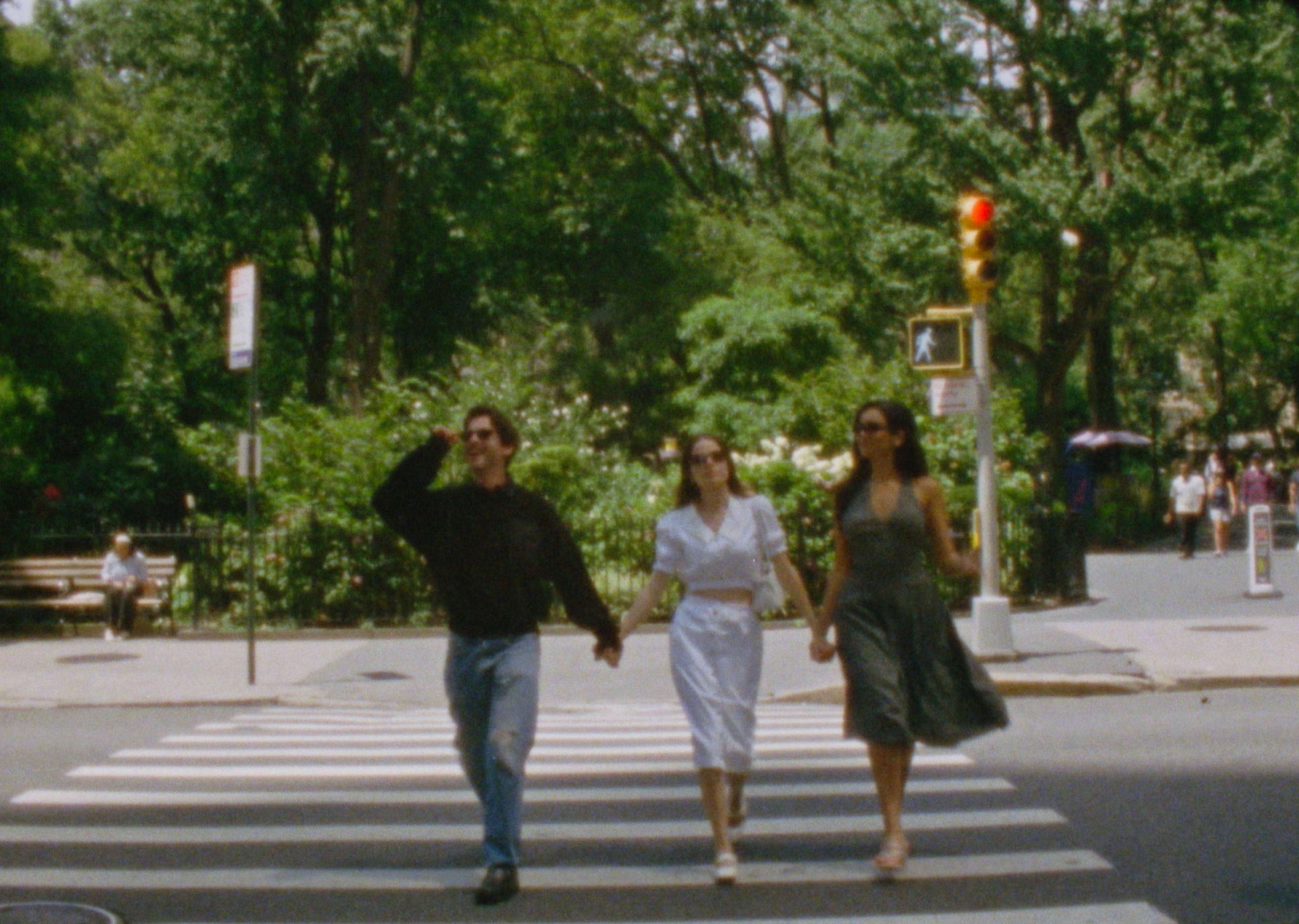 Molly Gordon and two friends walk hand-in-hand through a city crosswalk under summer trees — film still by Sarah Davis.