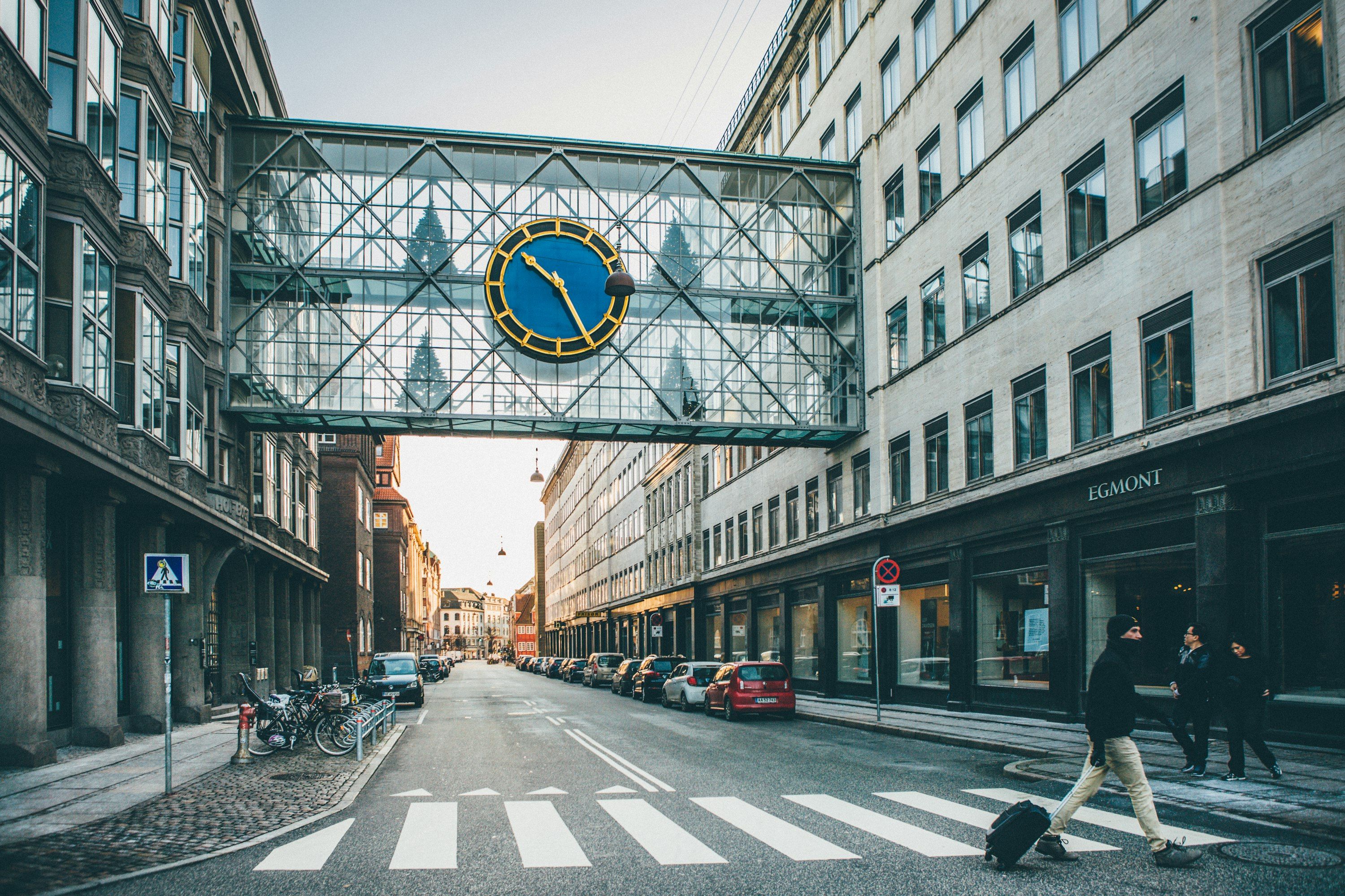 Folk krydser en gade mellem etageejendomme i København i lavt sollys