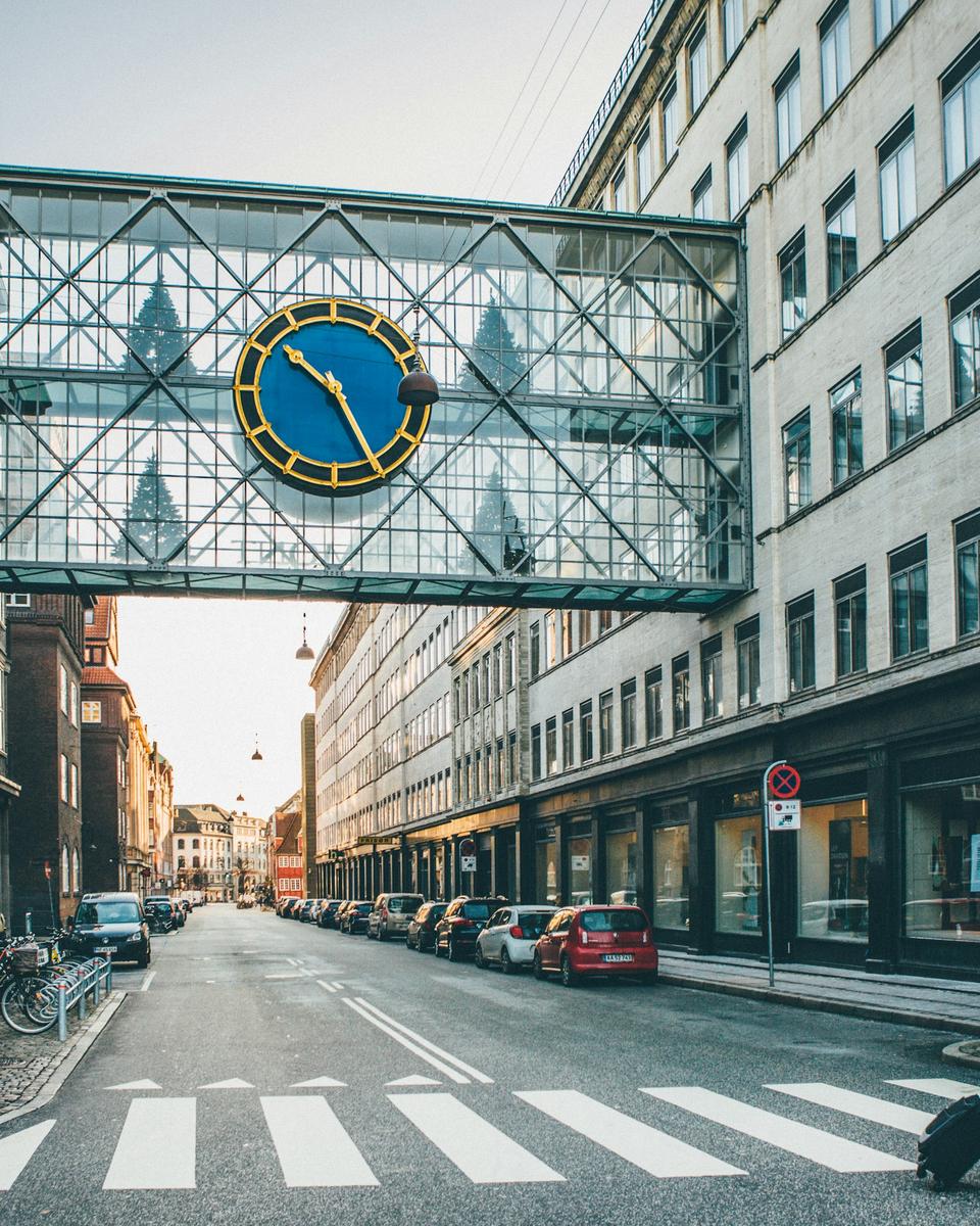 Folk krydser en gade mellem etageejendomme i København i lavt sollys