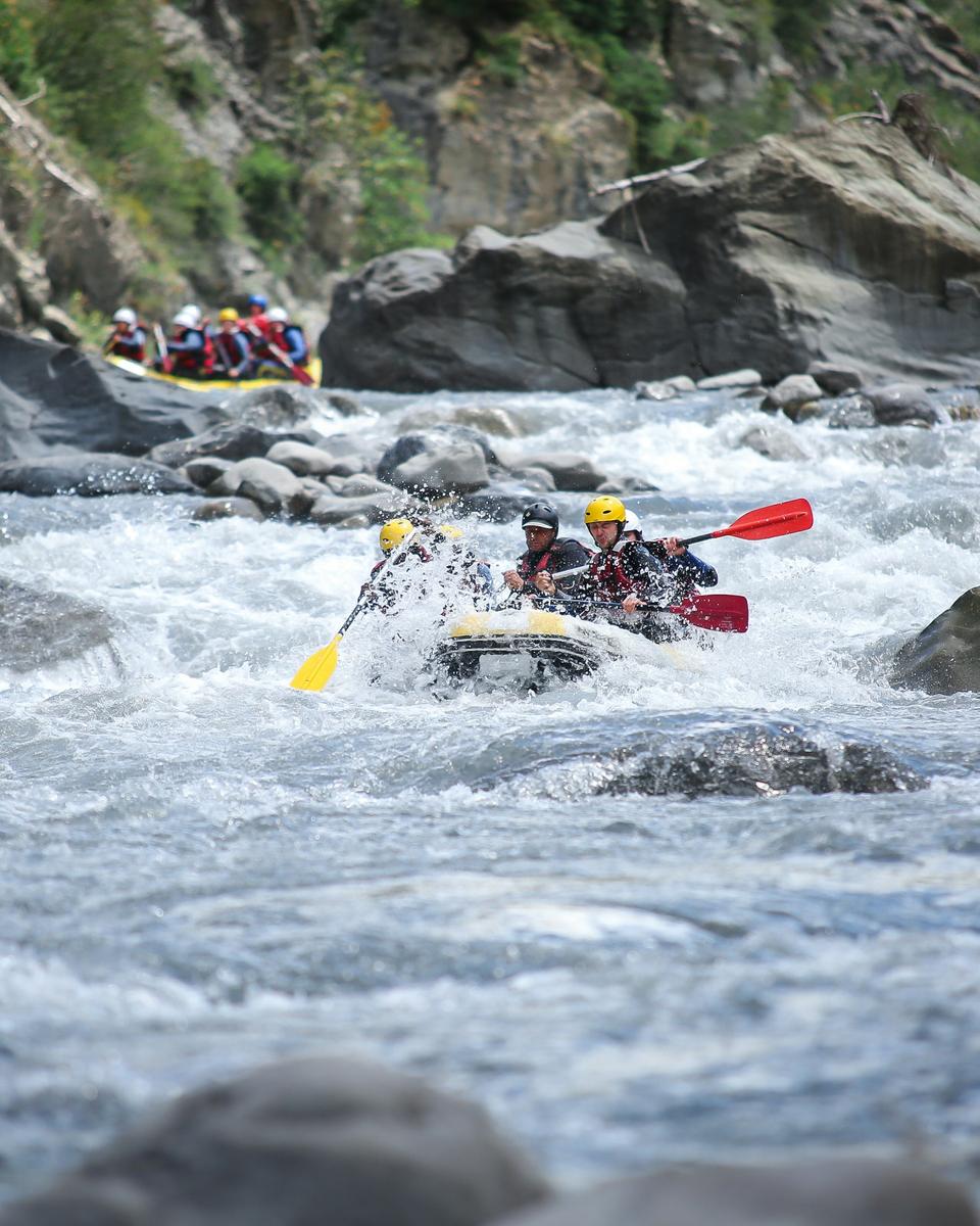 Gruppe med hjelme padler rafting gennem strømfald på en flod
