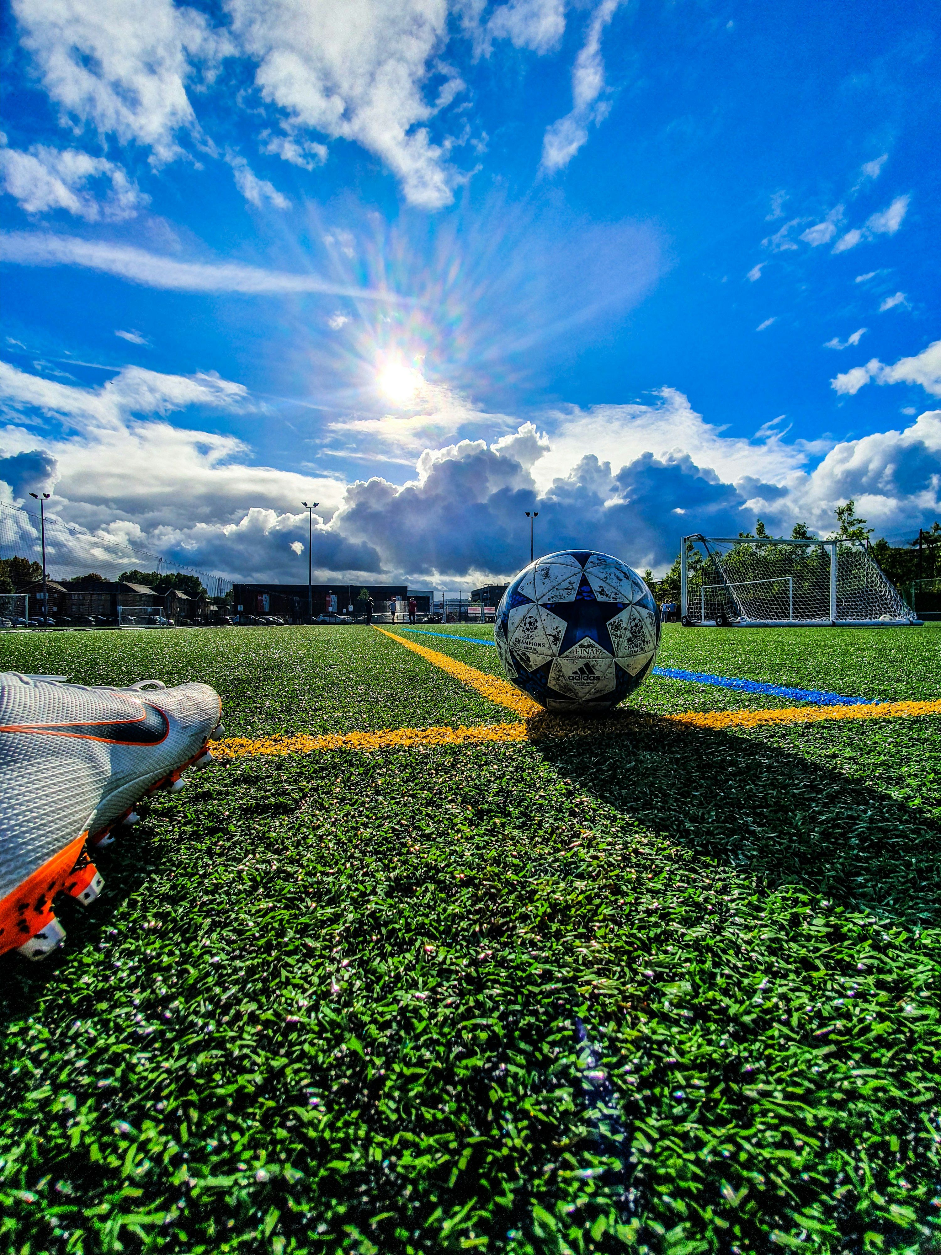 Fodbold på grøn bane i solskin under blå himmel