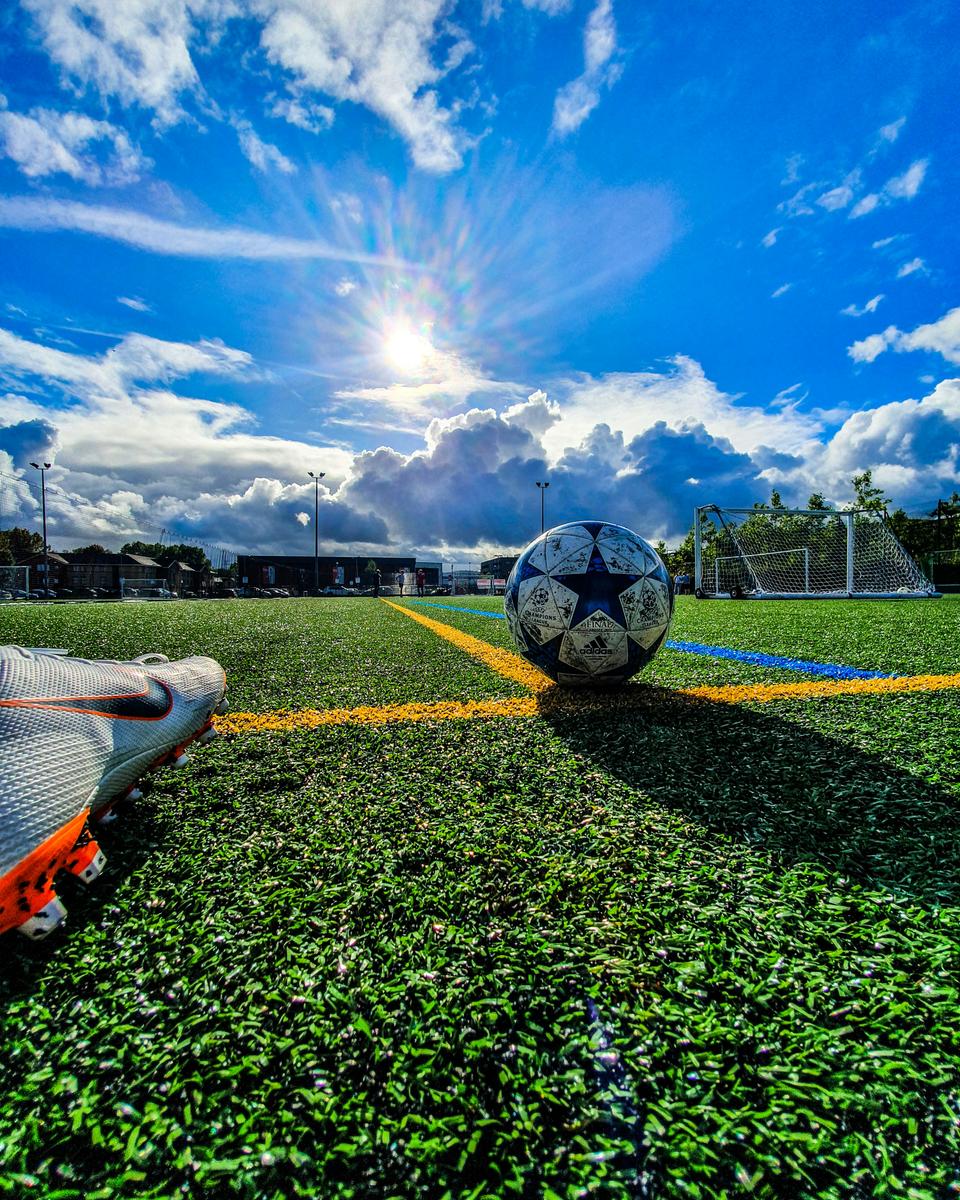 Fodbold på grøn bane i solskin under blå himmel