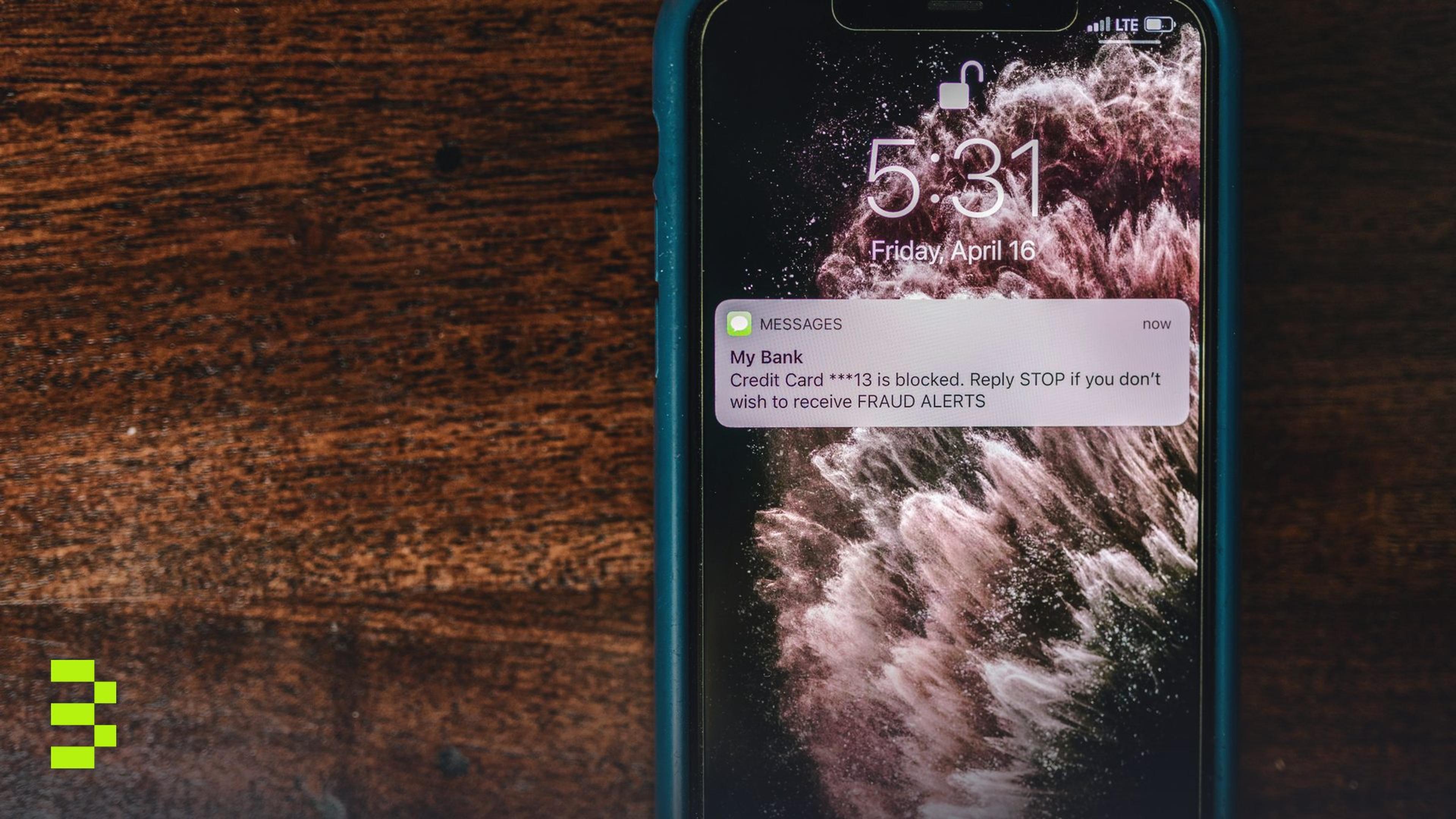 Close-up of smartphone displaying a fraud alert message on wooden surface.