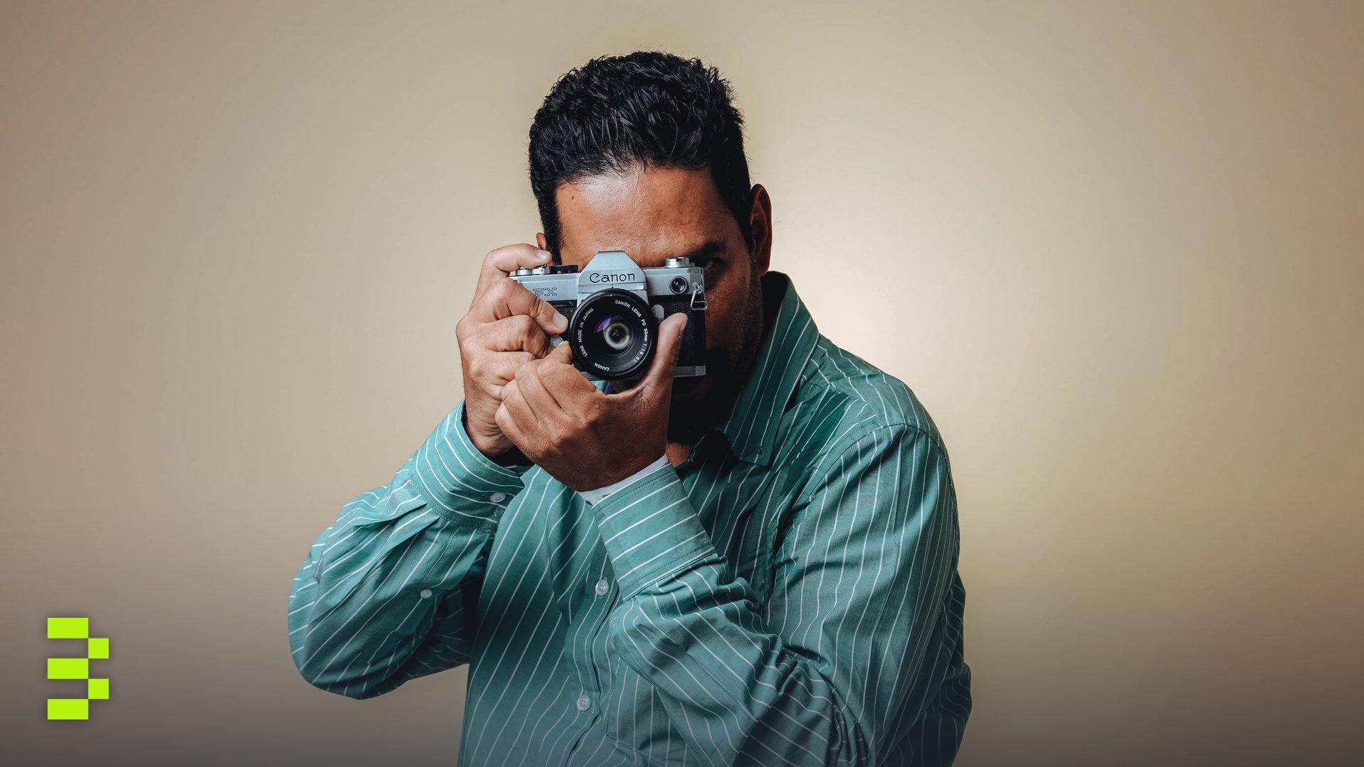 Man posing with a vintage camera in a studio setting wearing a striped green shirt.