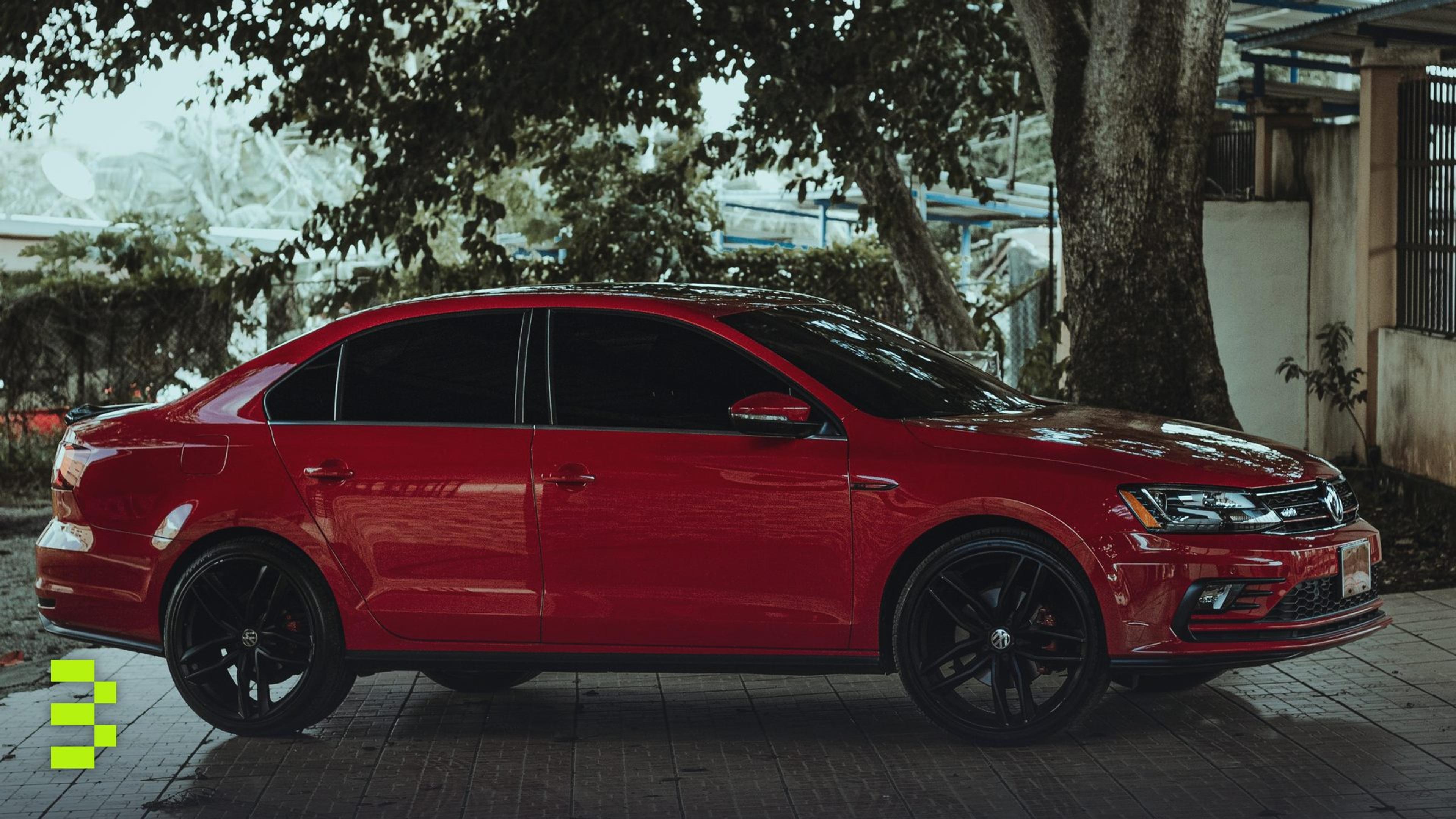 A striking red sedan parked under a tree on a paved surface.