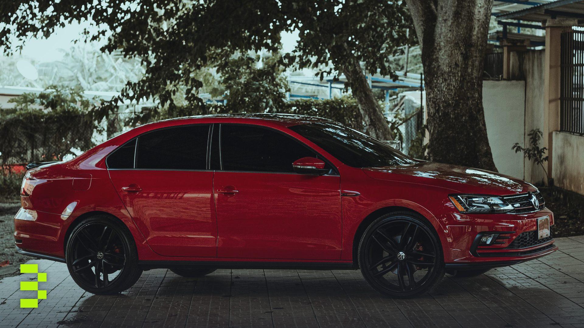 A striking red sedan parked under a tree on a paved surface.