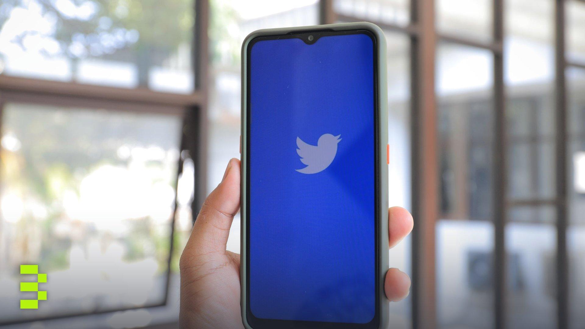 Hand holding a smartphone displaying the Twitter logo, indoors with natural light.