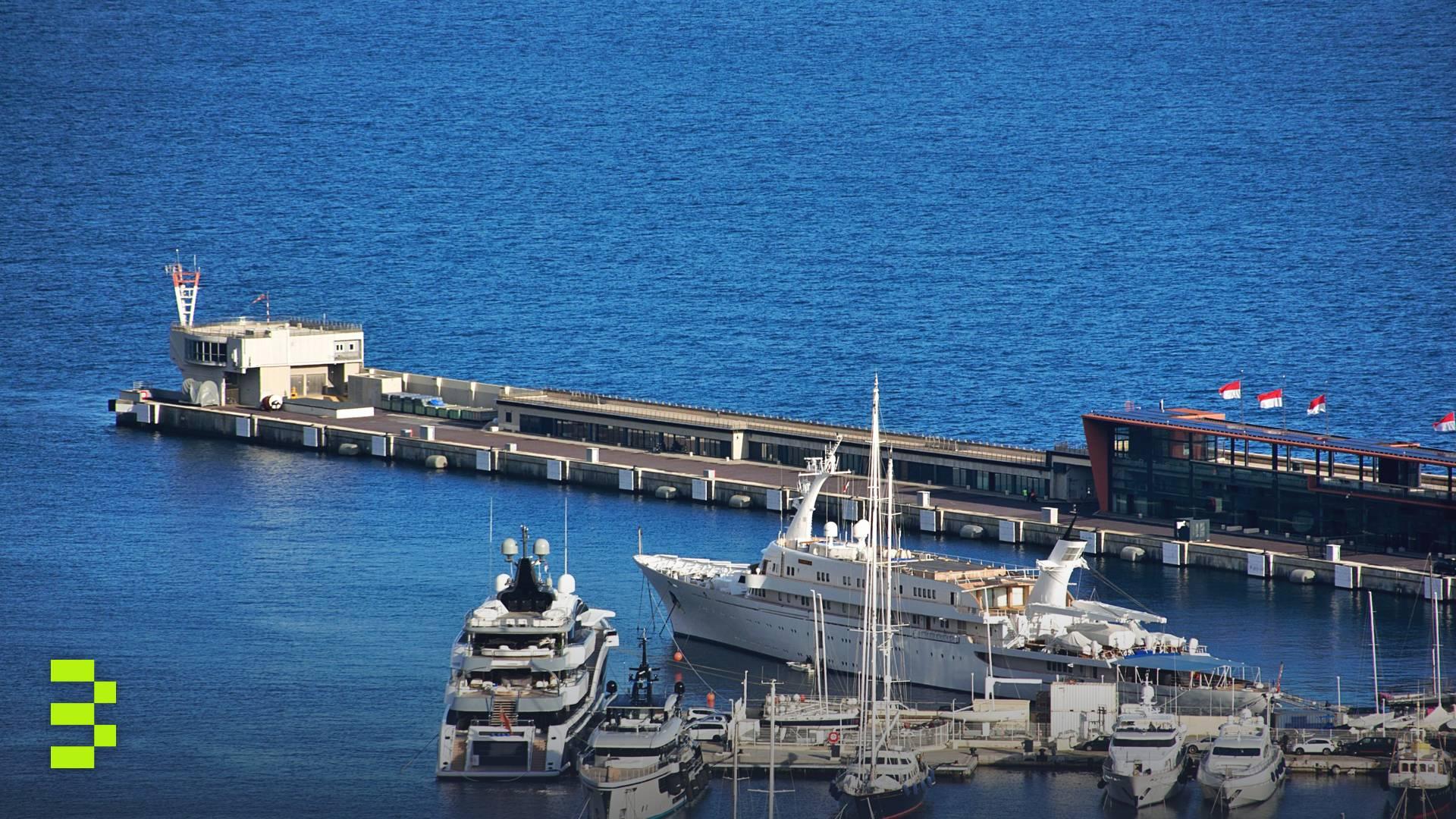Aerial view of luxury yachts docked at the marina in Monaco with vibrant blue sea.
