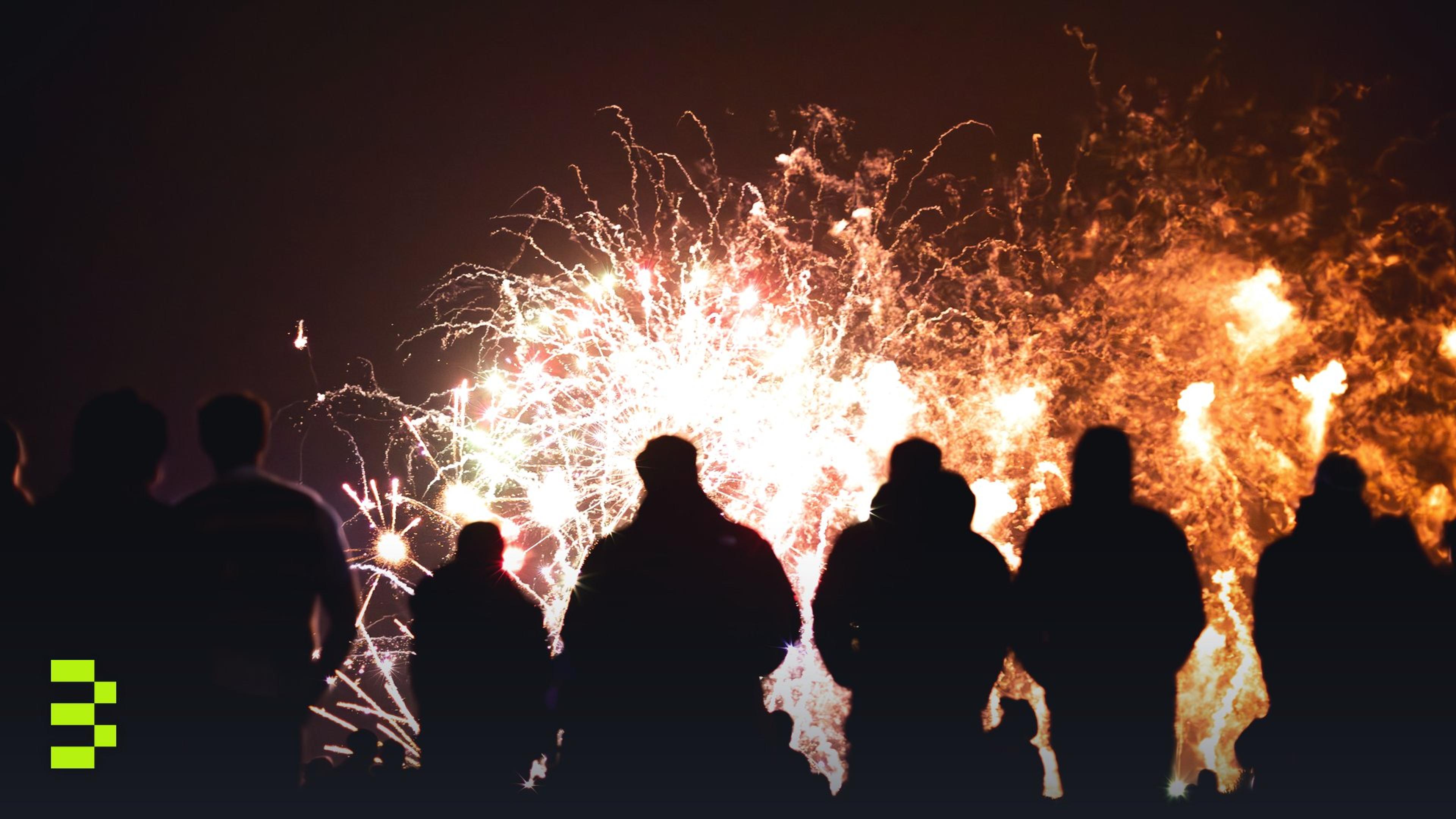 Silhouetted crowd watching a vibrant fireworks display in the night sky.