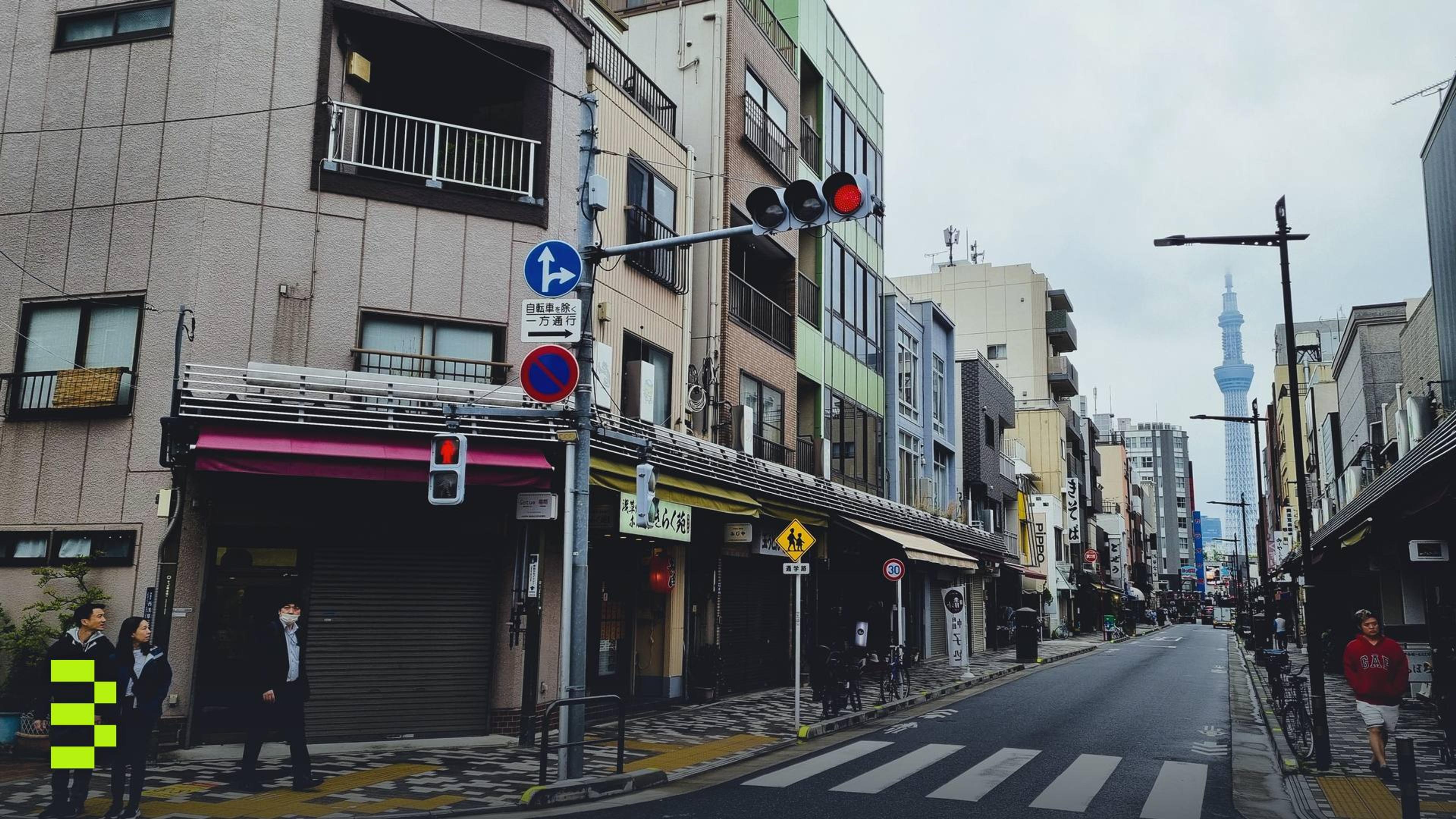 Street scene in Tokyo with pedestrians and the iconic Tokyo Skytree visible in the distance.