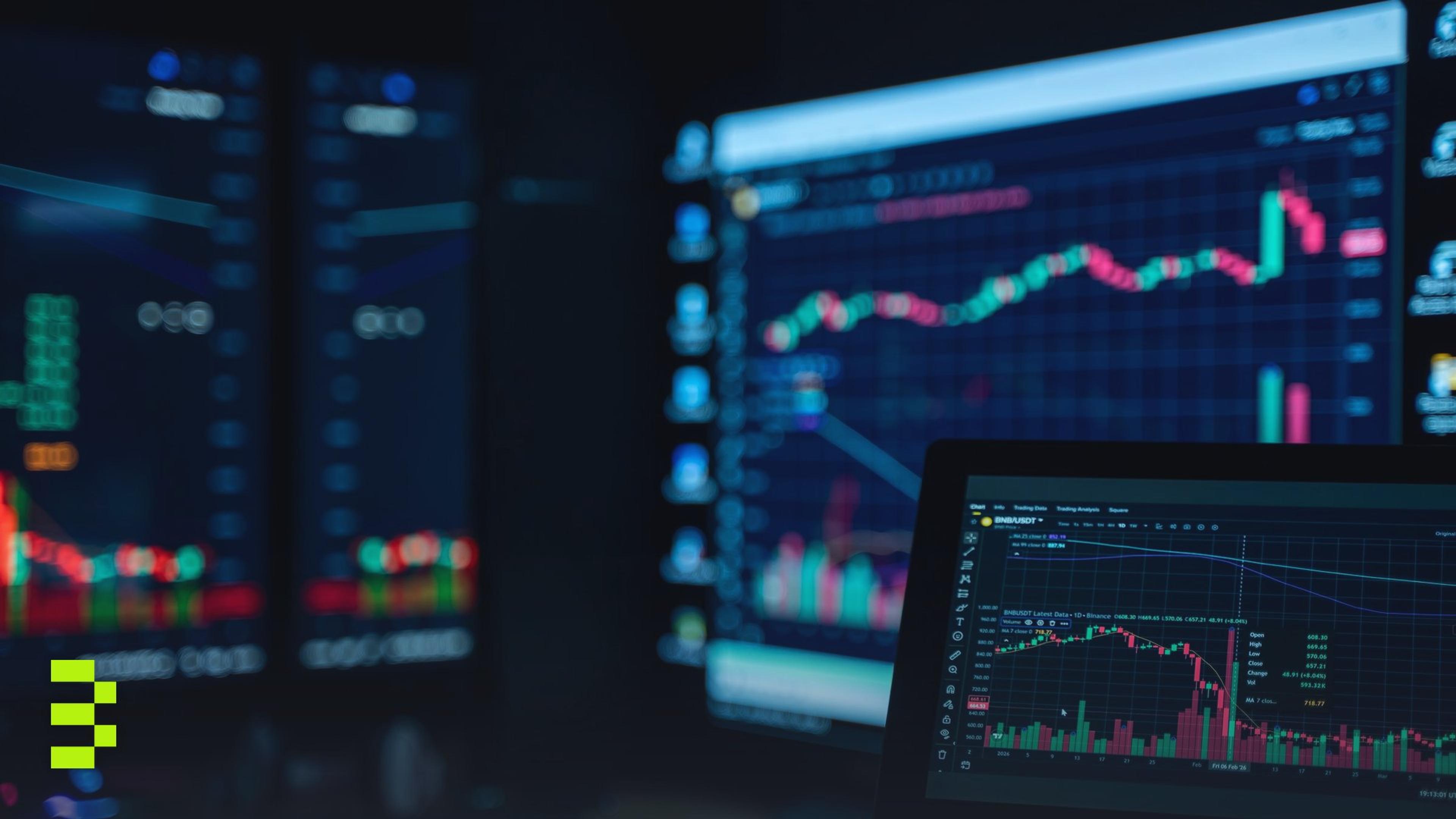 Stock market candlestick charts glowing on several monitors in a dark room.