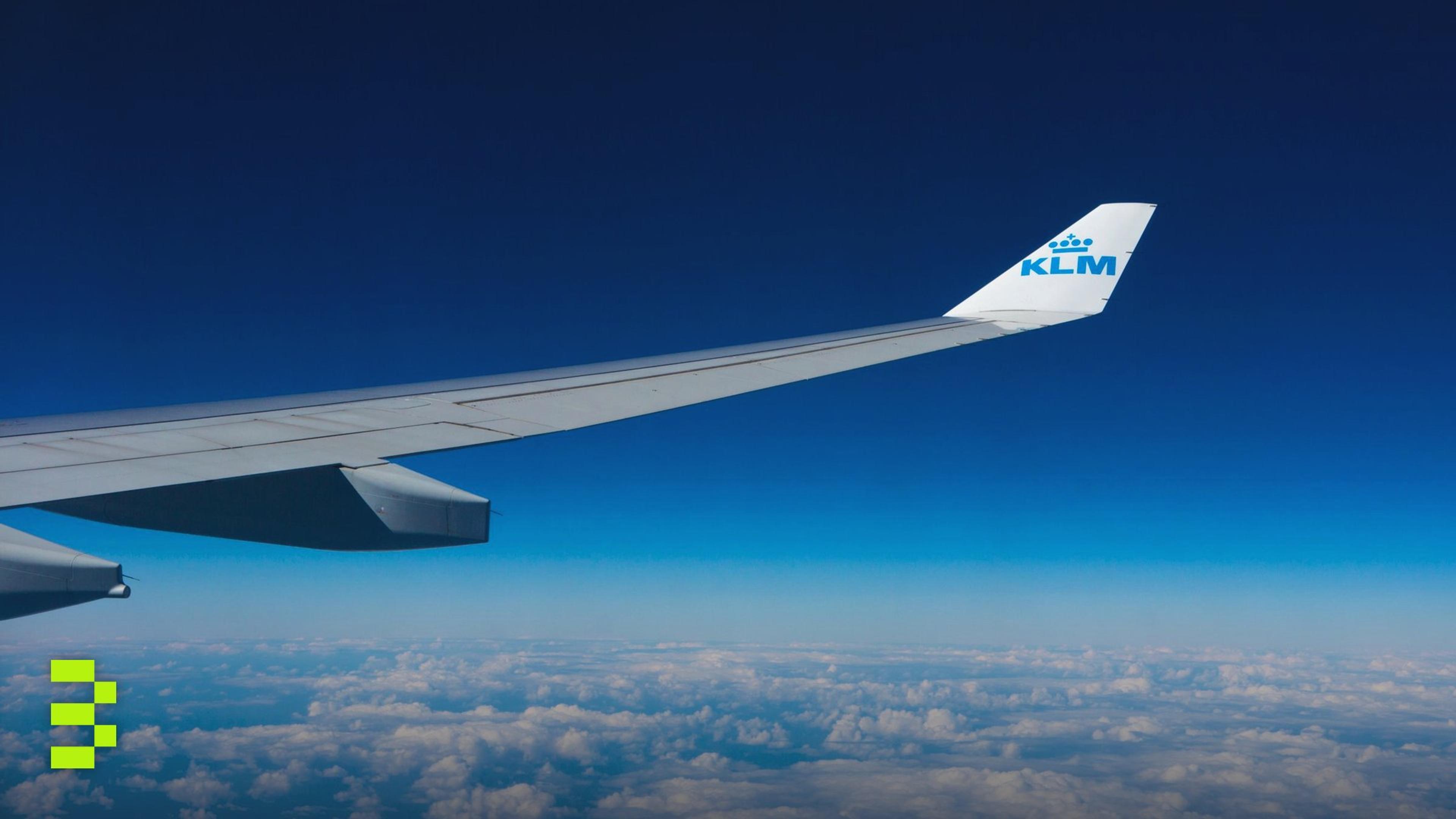 View of an airplane wing flying high above the clouds against a clear blue sky.