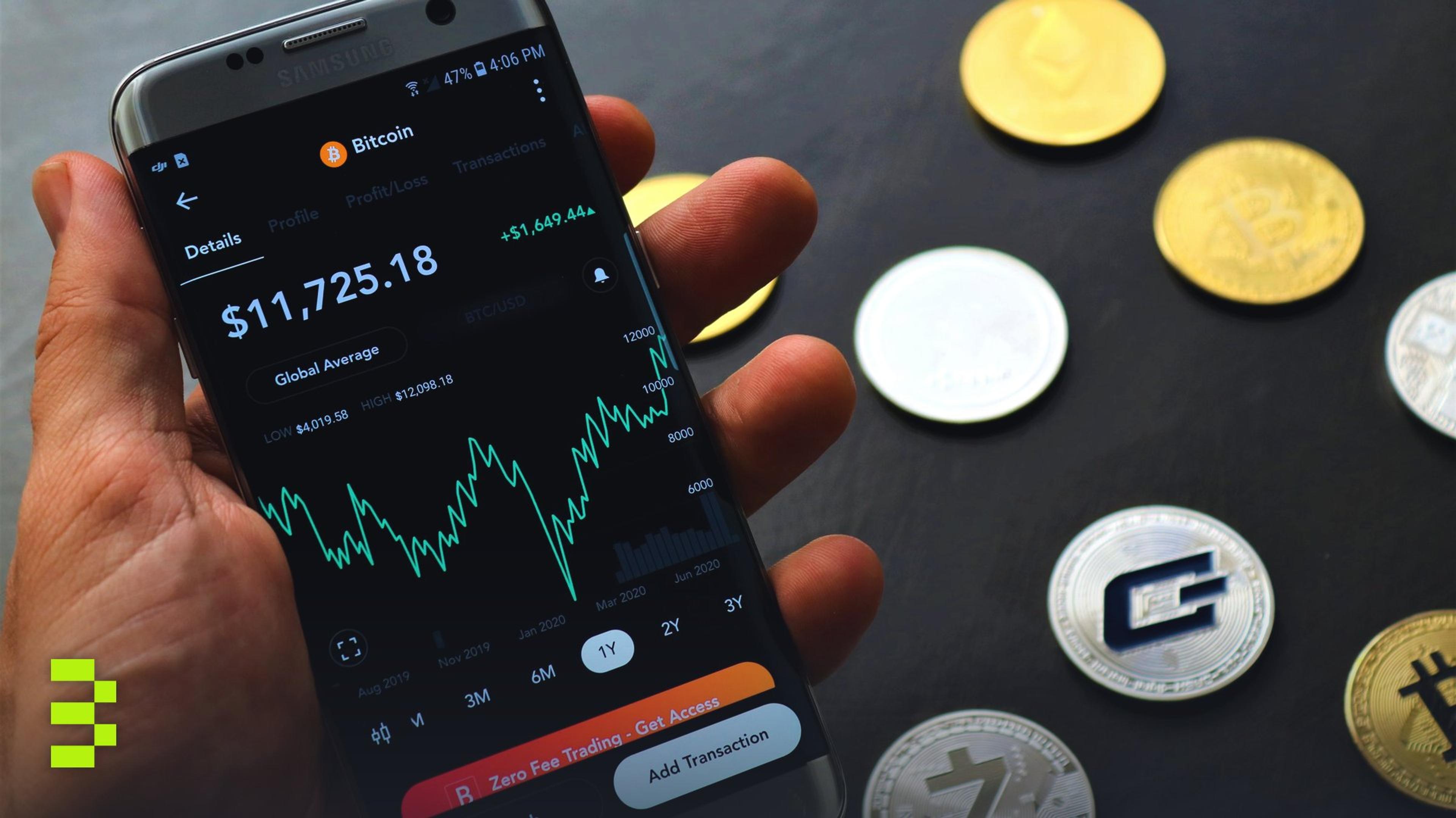 Close-up of a smartphone app showing Bitcoin trading details with crypto coins on a black surface.