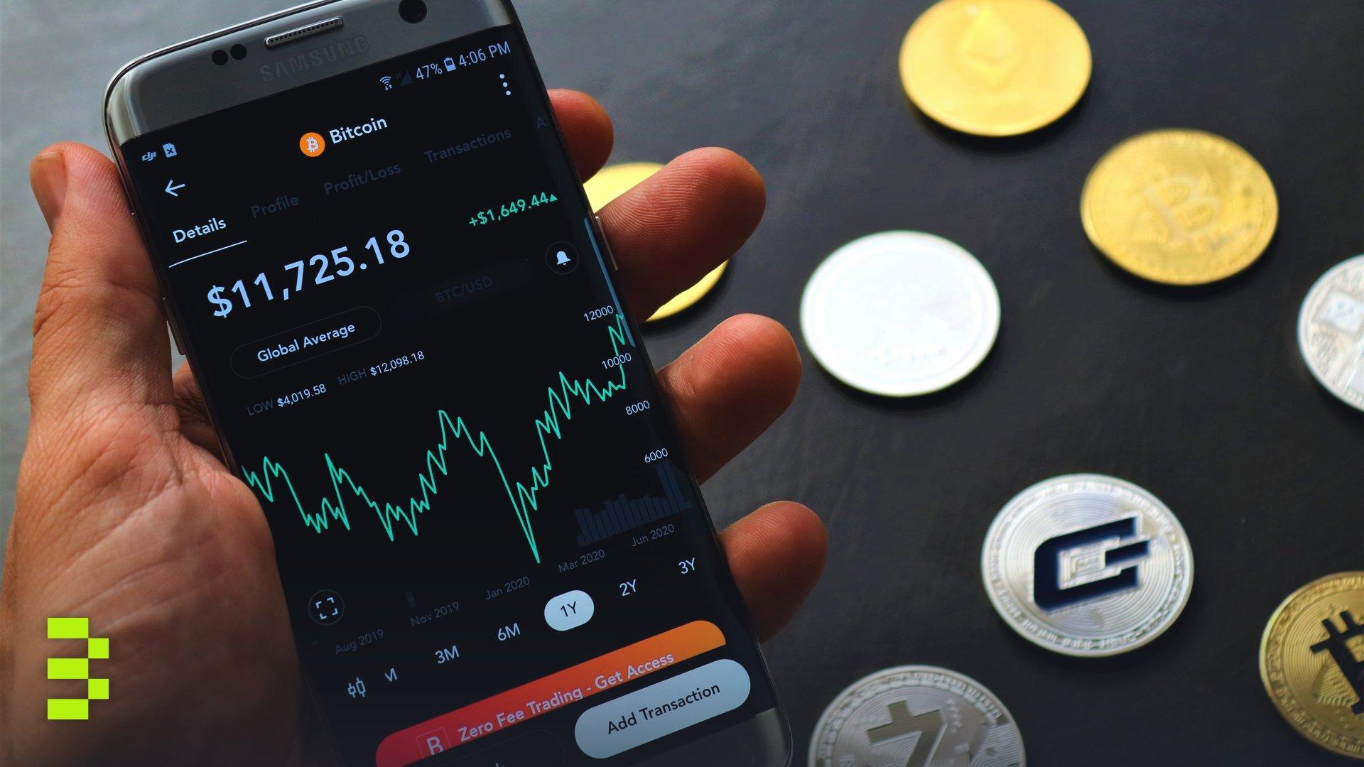 Close-up of a smartphone app showing Bitcoin trading details with crypto coins on a black surface.