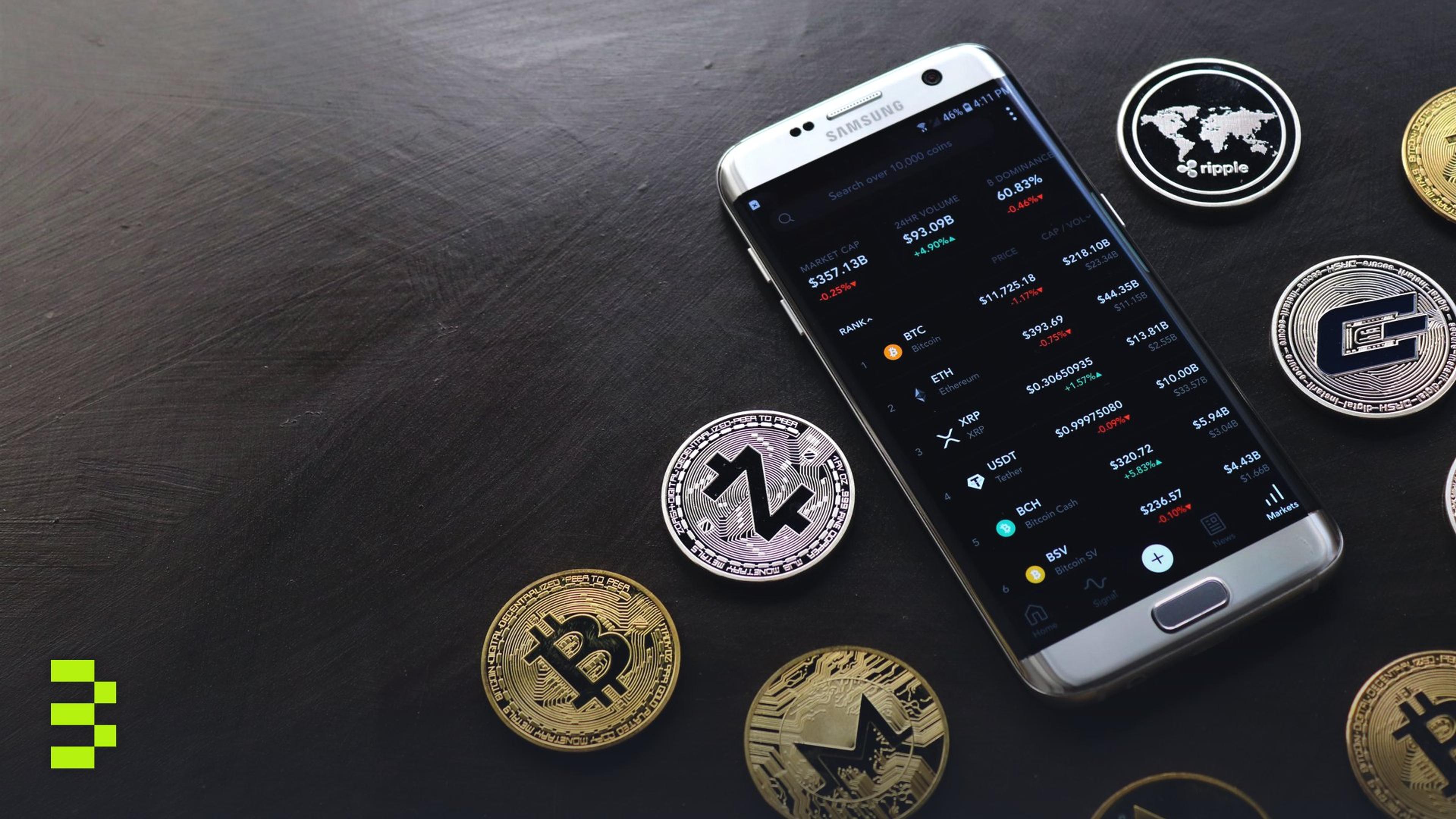 A collection of cryptocurrency coins and a smartphone displaying a digital trading platform.