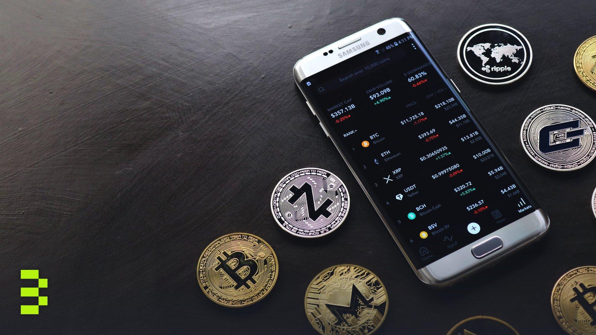 A collection of cryptocurrency coins and a smartphone displaying a digital trading platform.