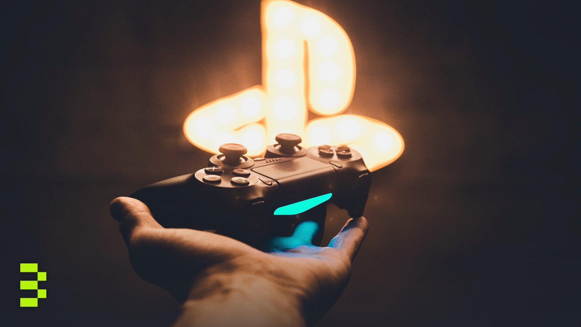 A hand holding a PlayStation controller with a blurred neon game symbol in the background.