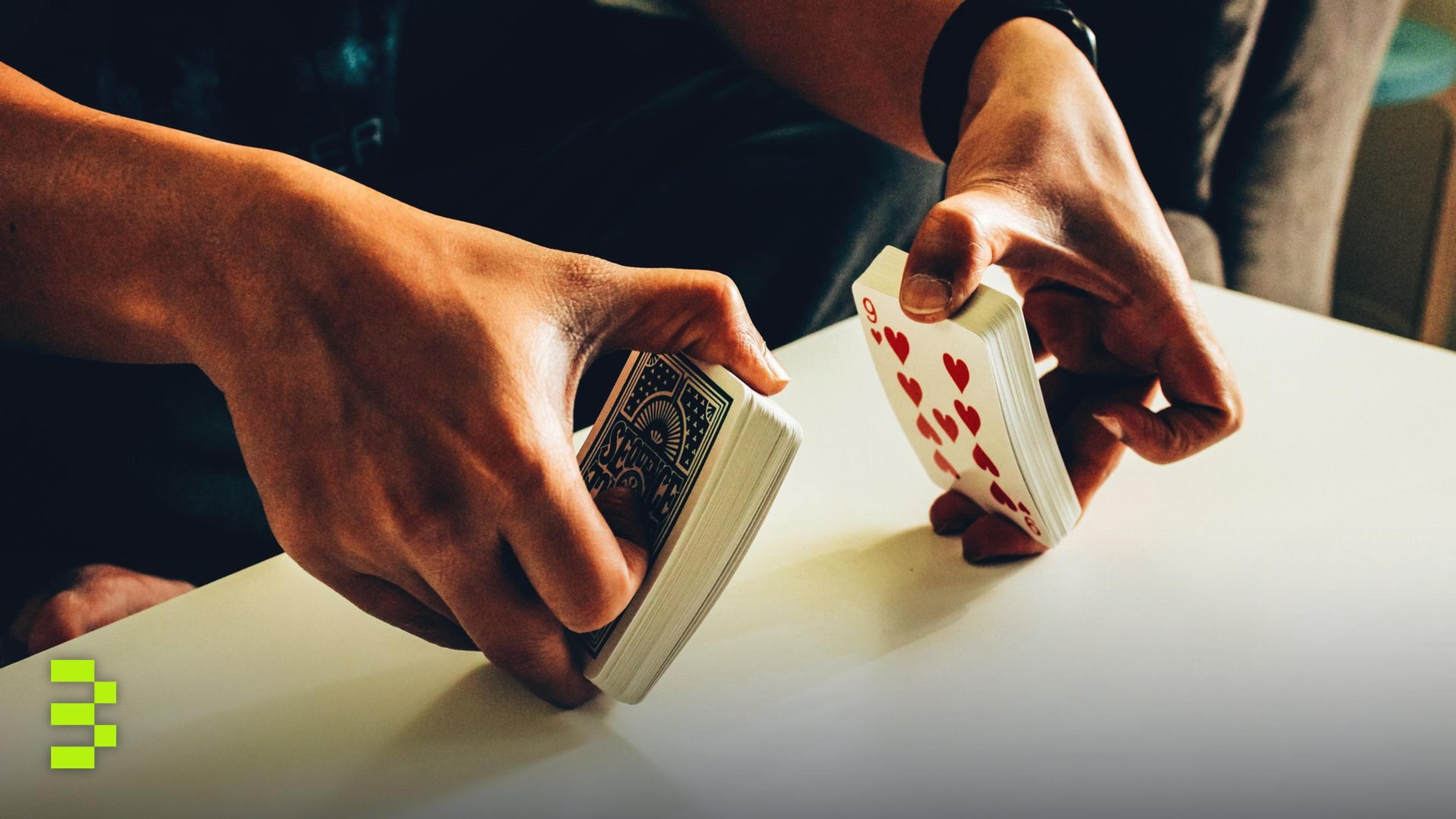 A person skillfully shuffles a deck of poker playing cards on a table indoors.