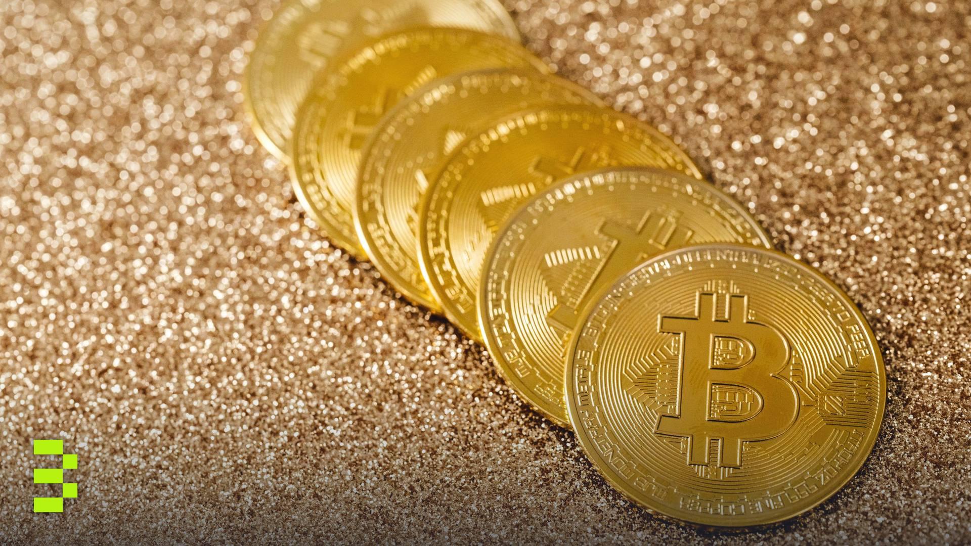 A stack of gold Bitcoin coins placed on a shimmering gold glitter background.