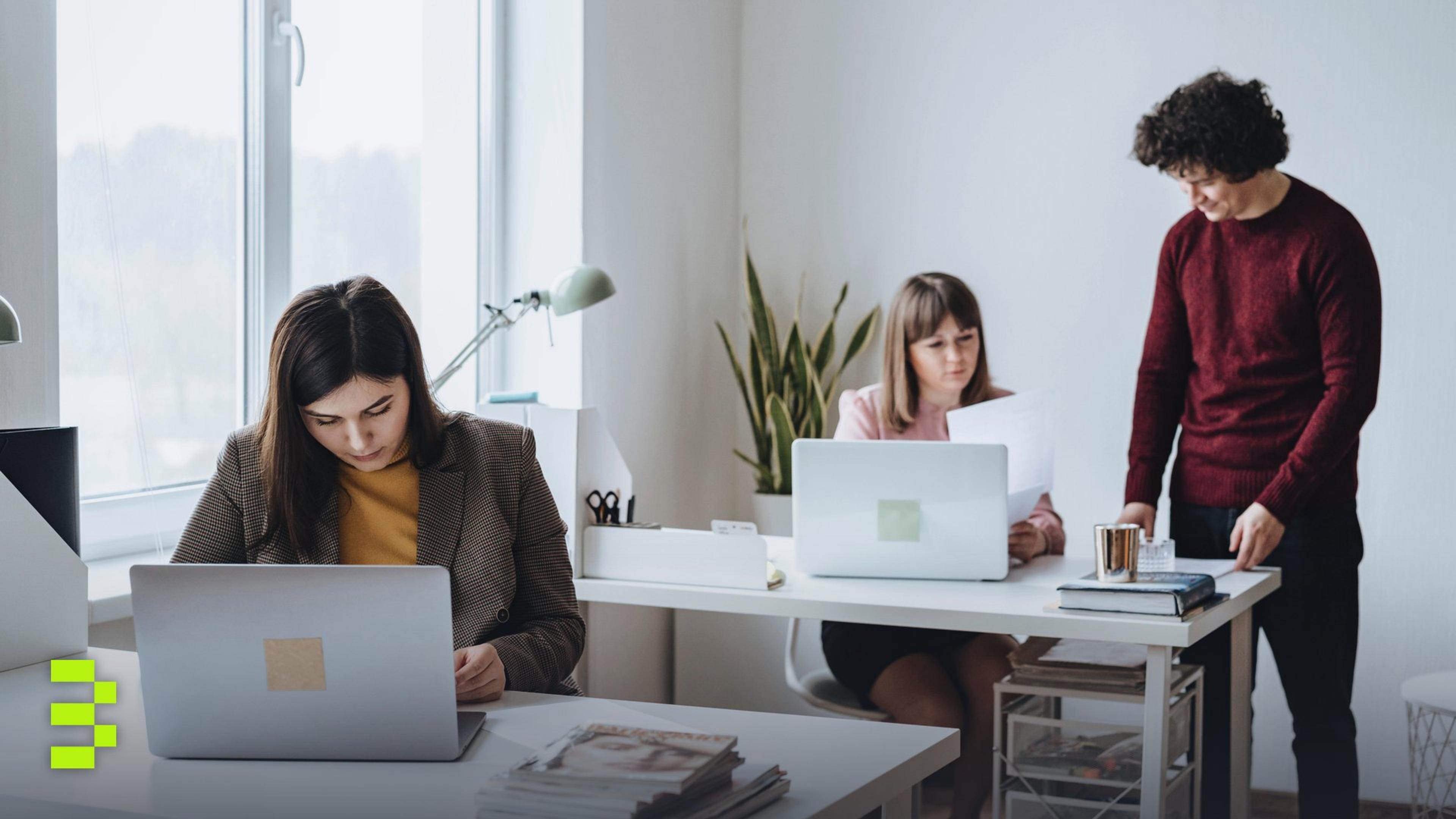 Group of colleagues working together in a bright, modern office space with laptops.