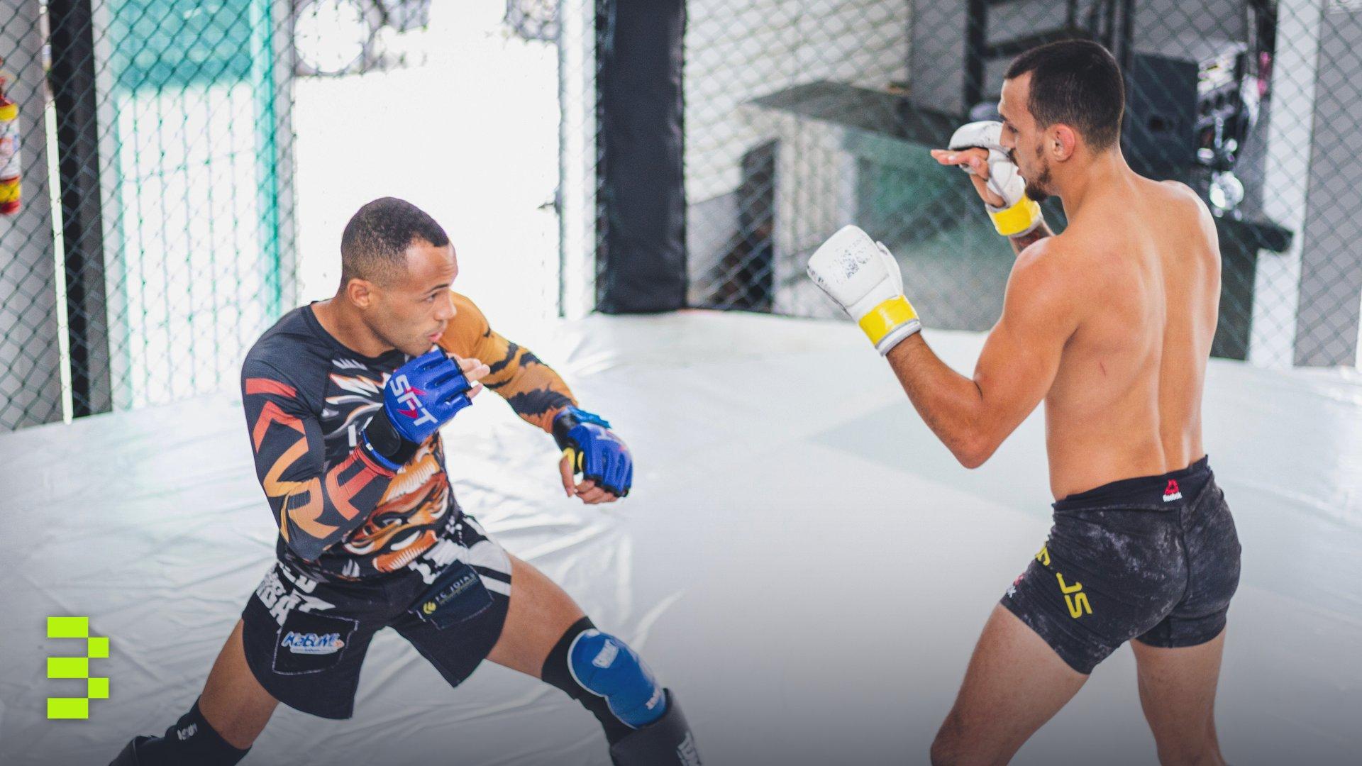 Two male fighters engaged in a mixed martial arts sparring session within a cage.
